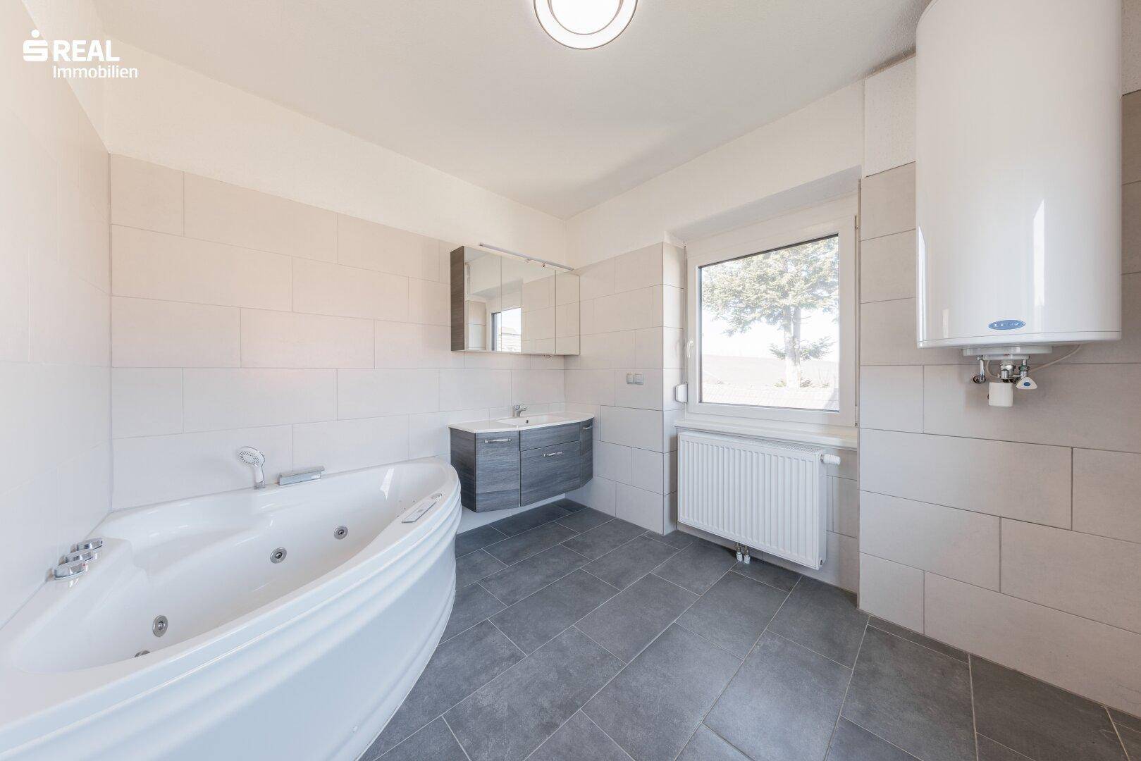 Modernes Badezimmer mit Whirlpool-Badewanne, Waschbecken und Fenster.