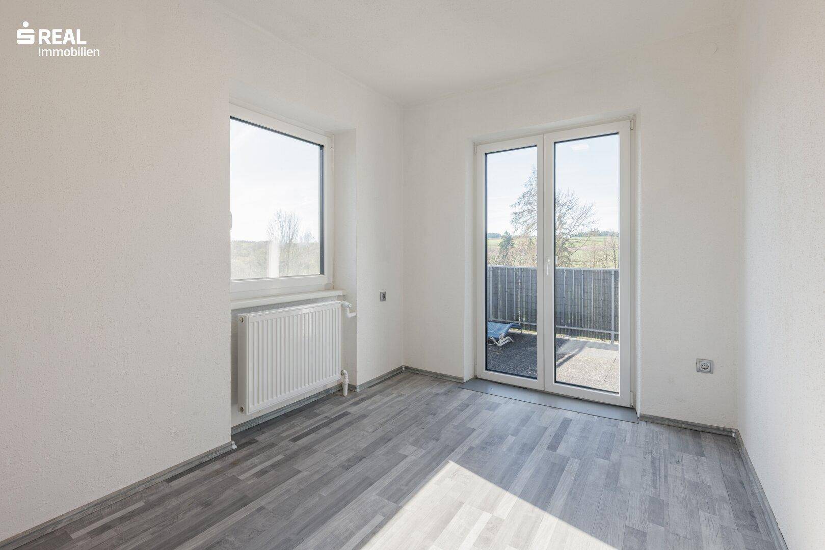 Helles Zimmer mit Laminatboden und Zugang zu einem Außenbereich.