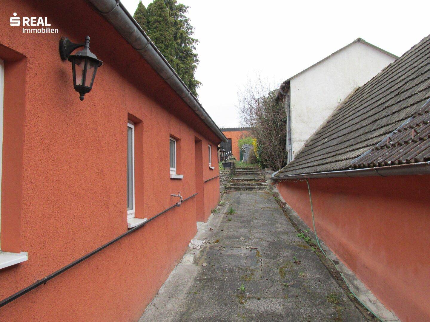 Seitenansicht des Hauses mit schmalem Zugangsweg und Außenbeleuchtung.