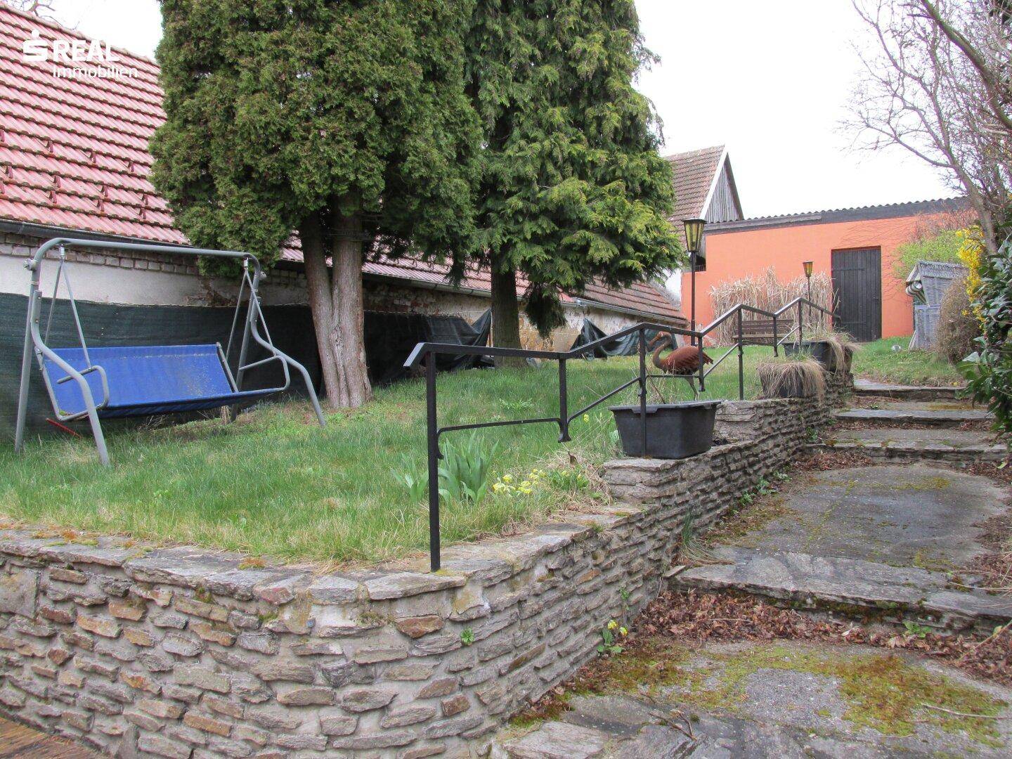 Garten mit Steintreppen, Rasenfläche und einer Steinmauer.