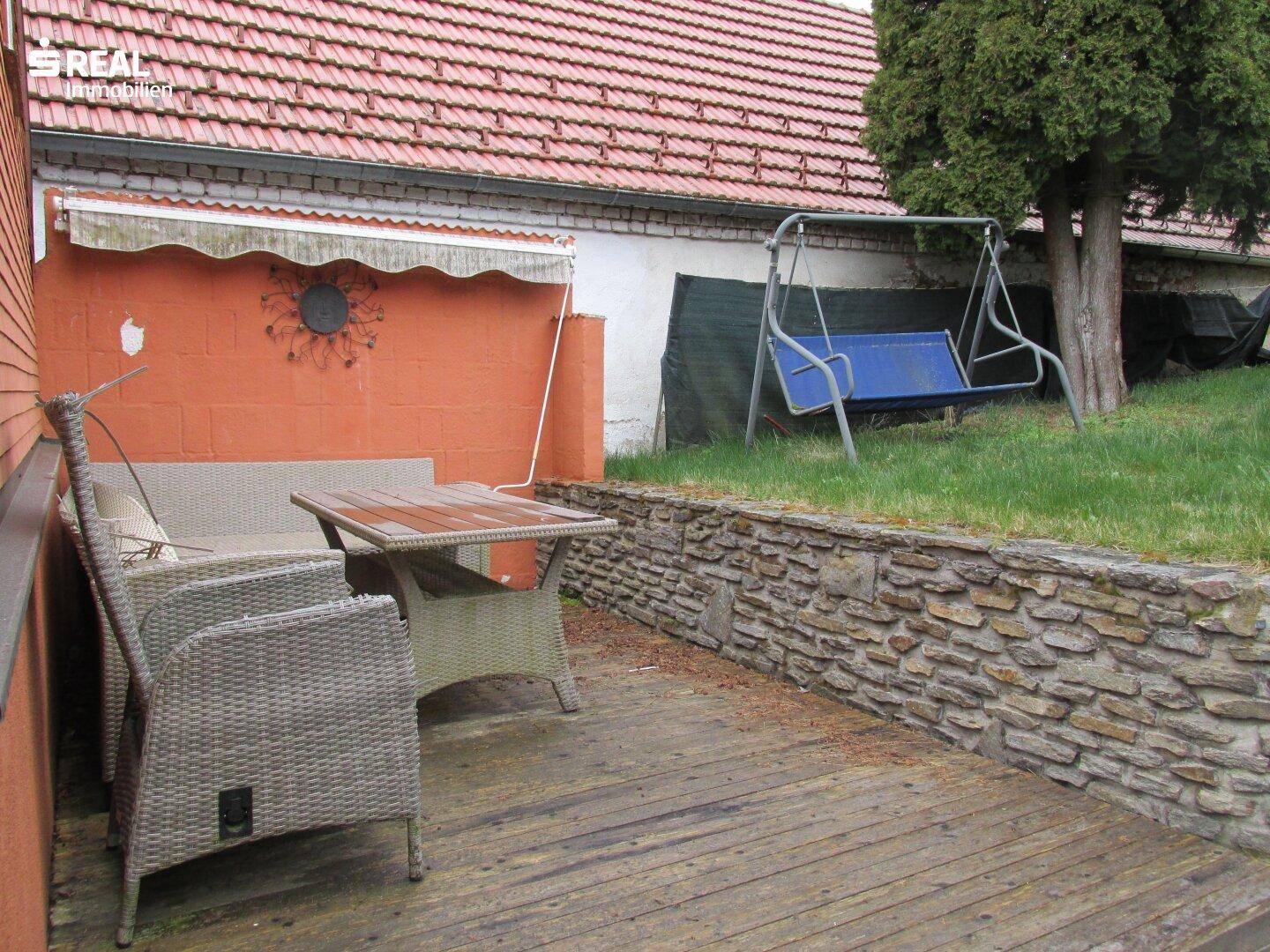 Holzterrasse mit Gartenmöbeln und angrenzender Rasenfläche mit Schaukel.