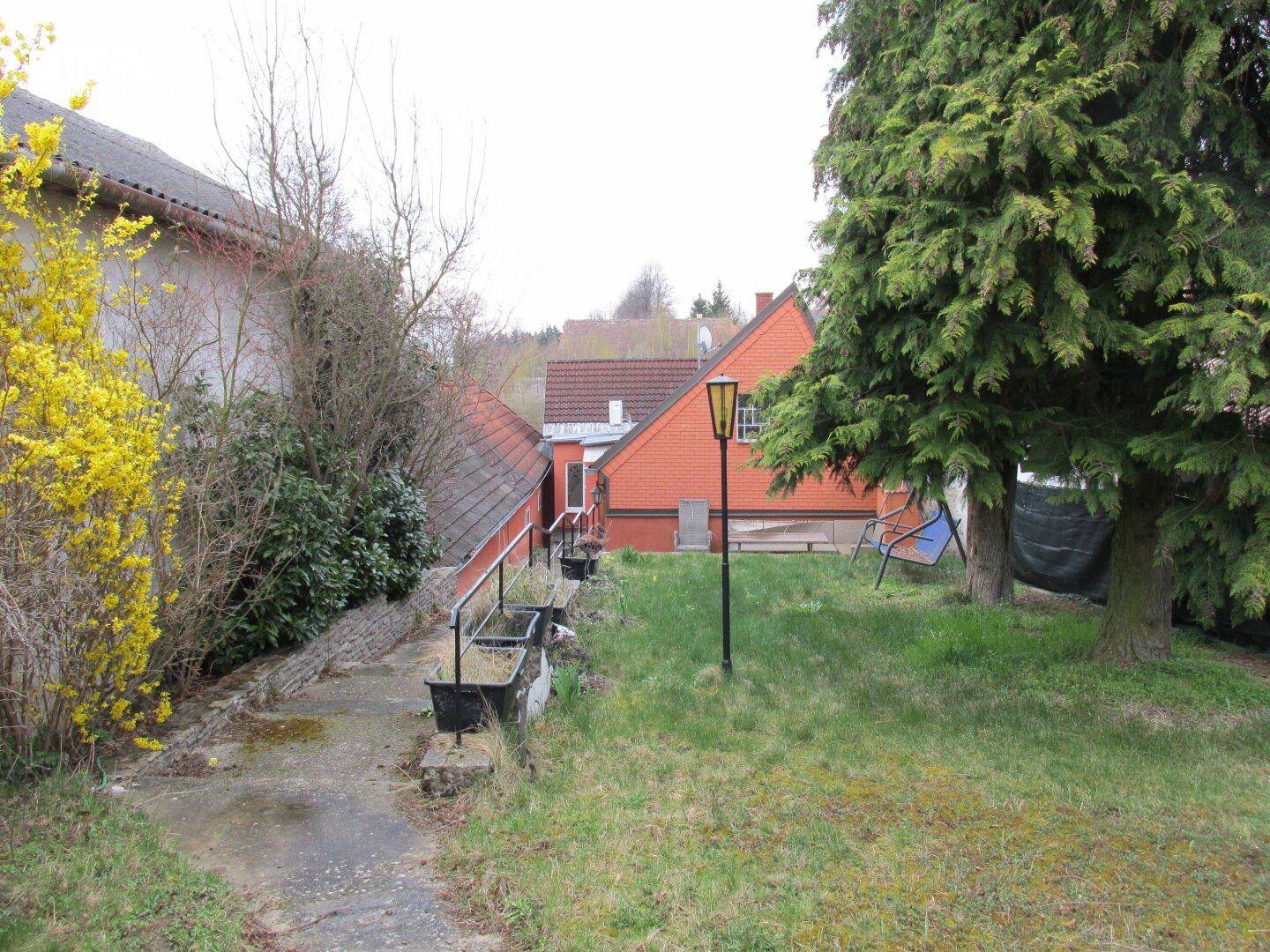 Gartenweg mit Bäumen und Sträuchern, der zu einem weiteren Bereich des Grundstücks führt.