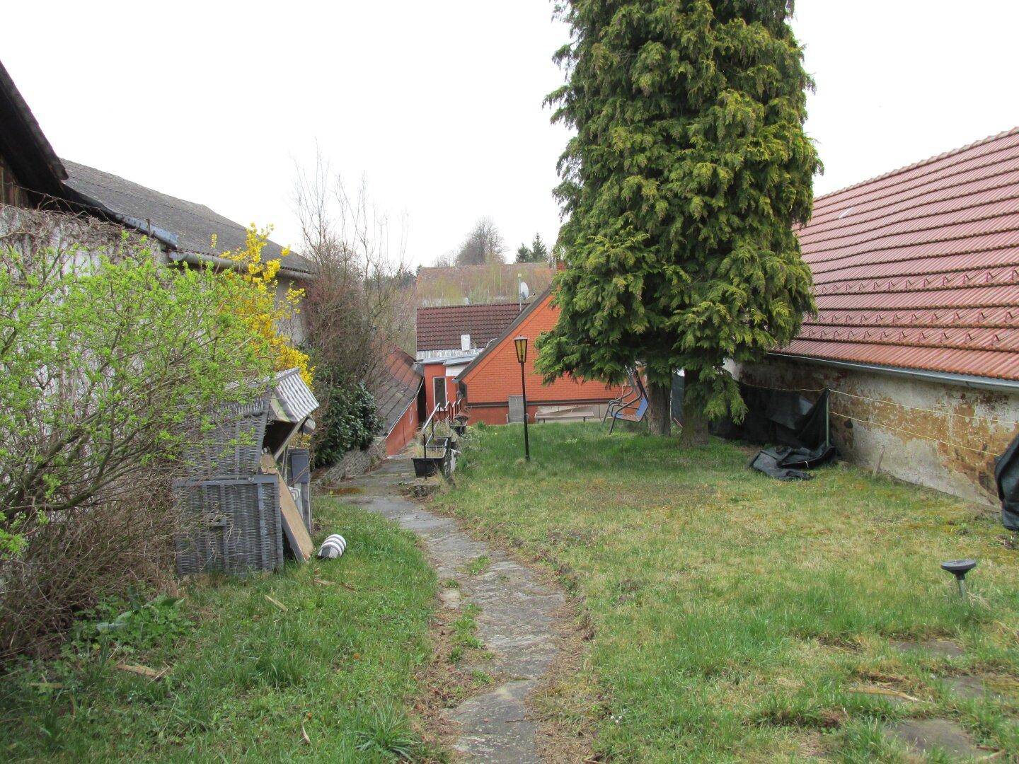 Gepflasterter Gartenweg umgeben von Rasen und Bäumen, mit Blick auf die Umgebung.
