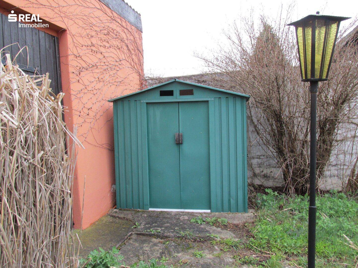 Grüner Metallschuppen im Gartenbereich, ideal zur Aufbewahrung von Gartengeräten.