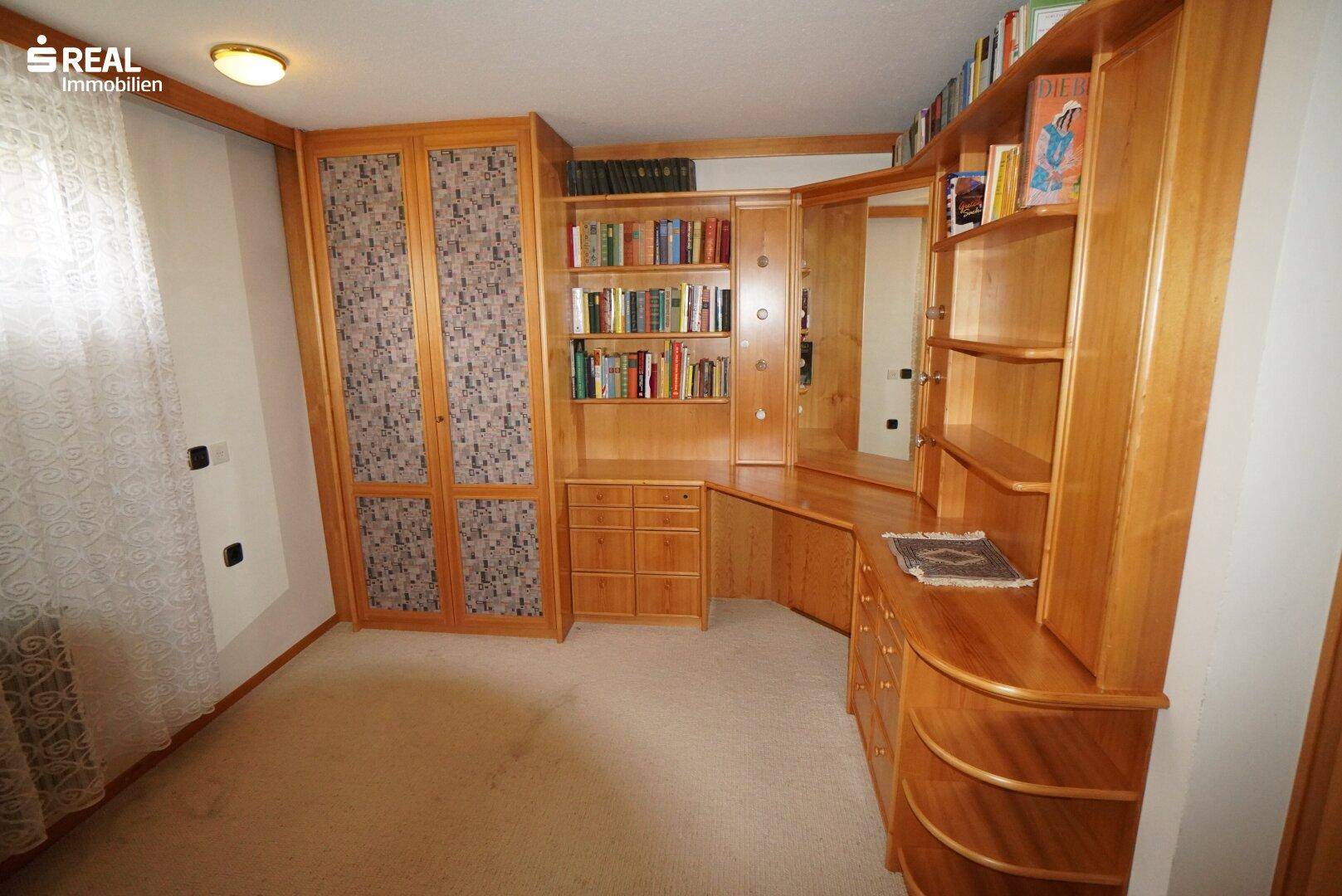 Arbeitszimmer mit umfangreichen Holzregalen, Schreibtisch und Teppichboden.
