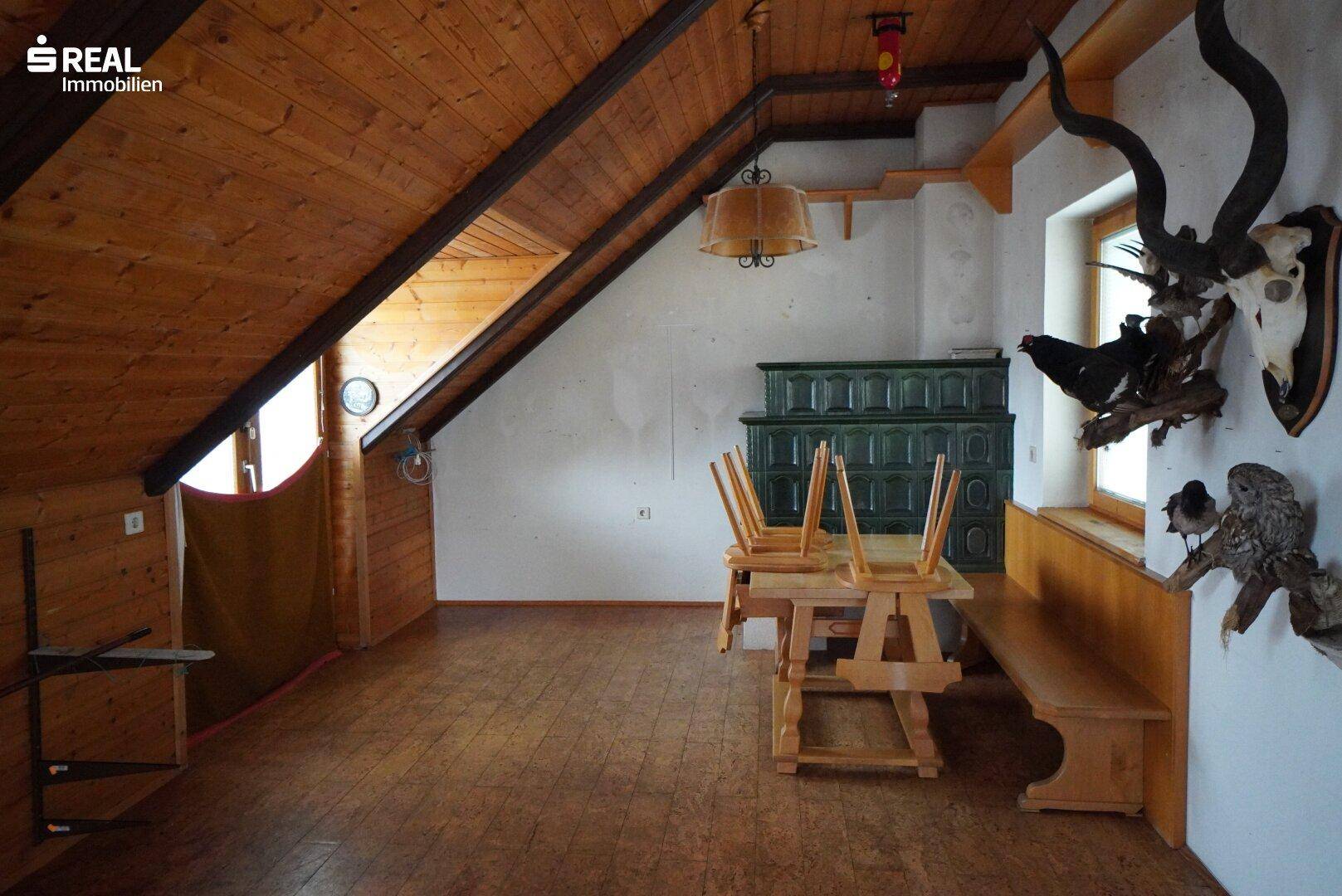 Rustikaler Dachbodenraum mit Holzbalken, Kachelofen, Holzmöbeln und Hirschgeweih-Dekoration.