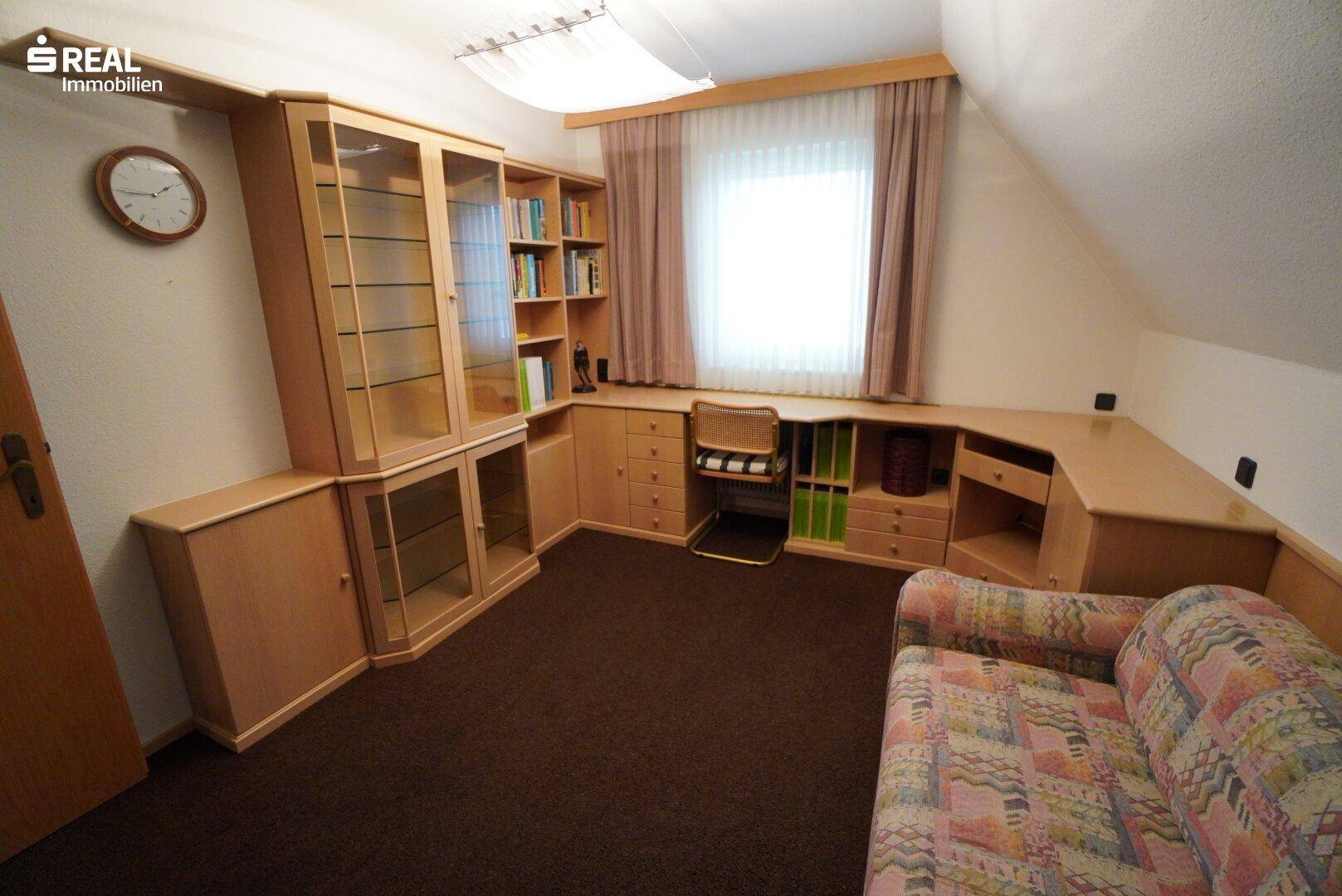 Gemütliches Arbeitszimmer mit maßgefertigten Holzmöbeln, Schreibtisch und Sofa unter Dachschräge.