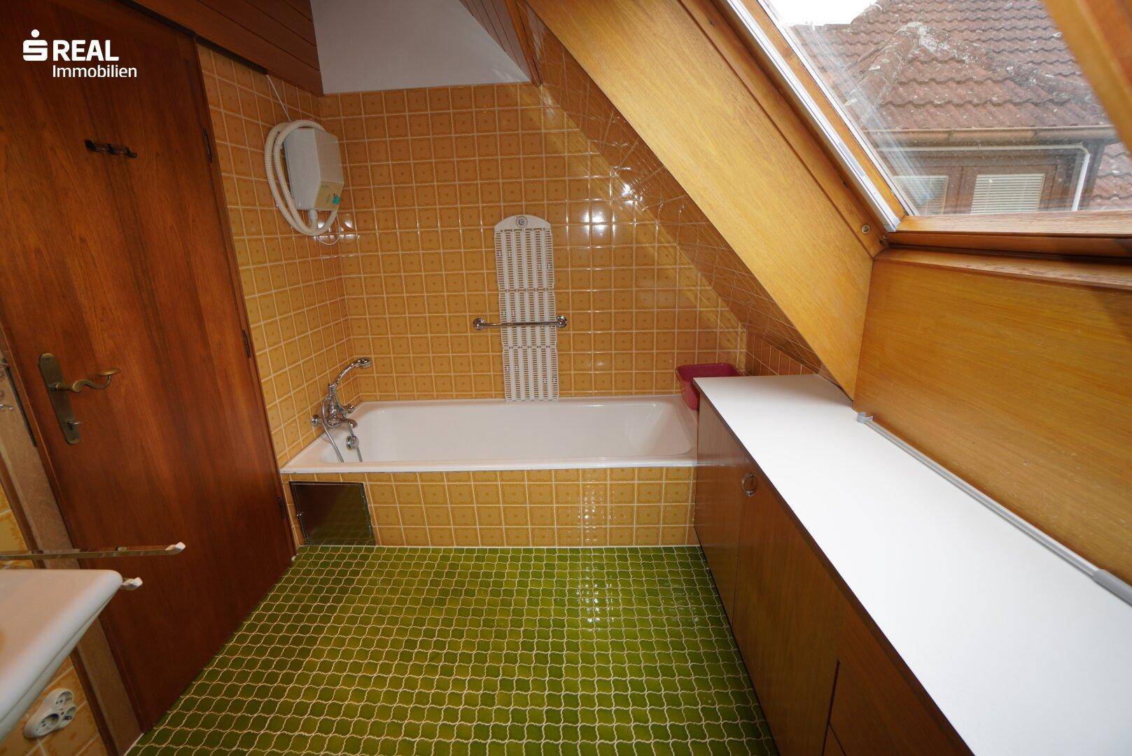 Badezimmer mit gelben Wandfliesen, grünen Bodenfliesen, Badewanne und Dachfenster.