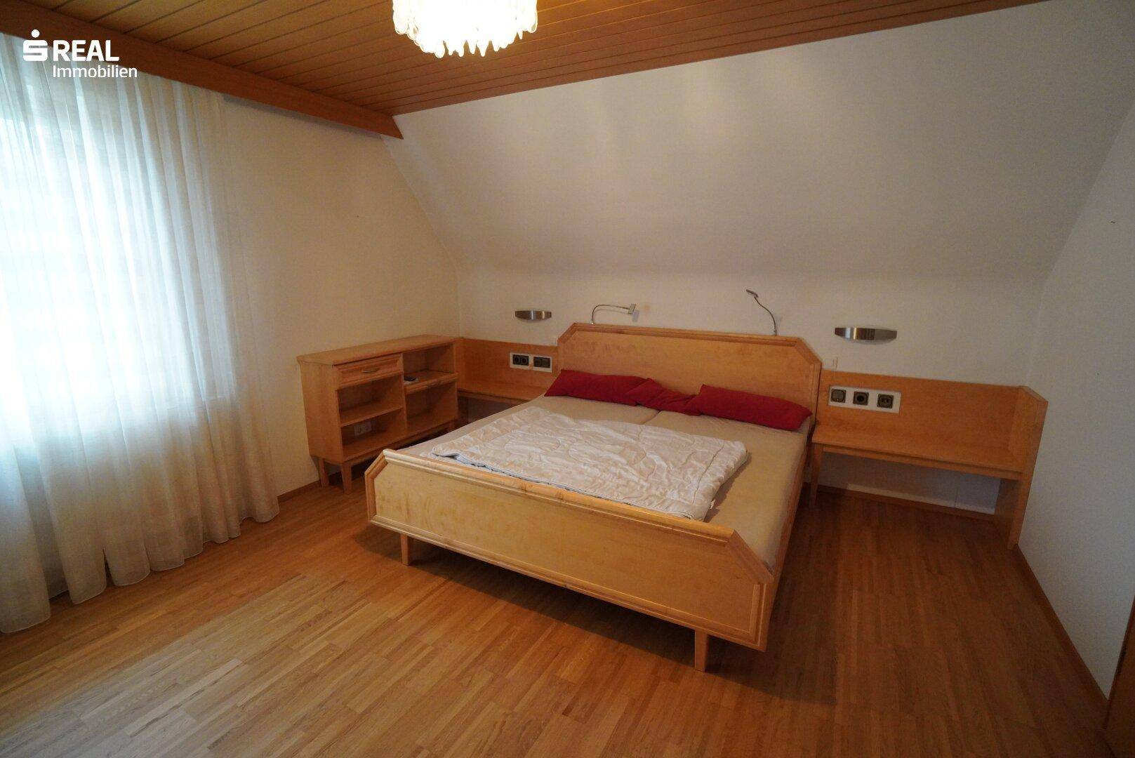 Helles Schlafzimmer mit Holzbett, Holzdecke und Dielenboden unter einer Dachschräge.