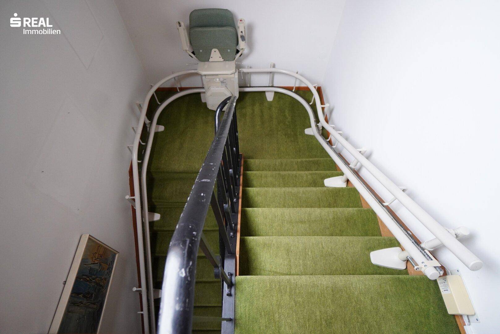 Treppenhaus mit grünem Teppichboden und installiertem Treppenlift für Barrierefreiheit.