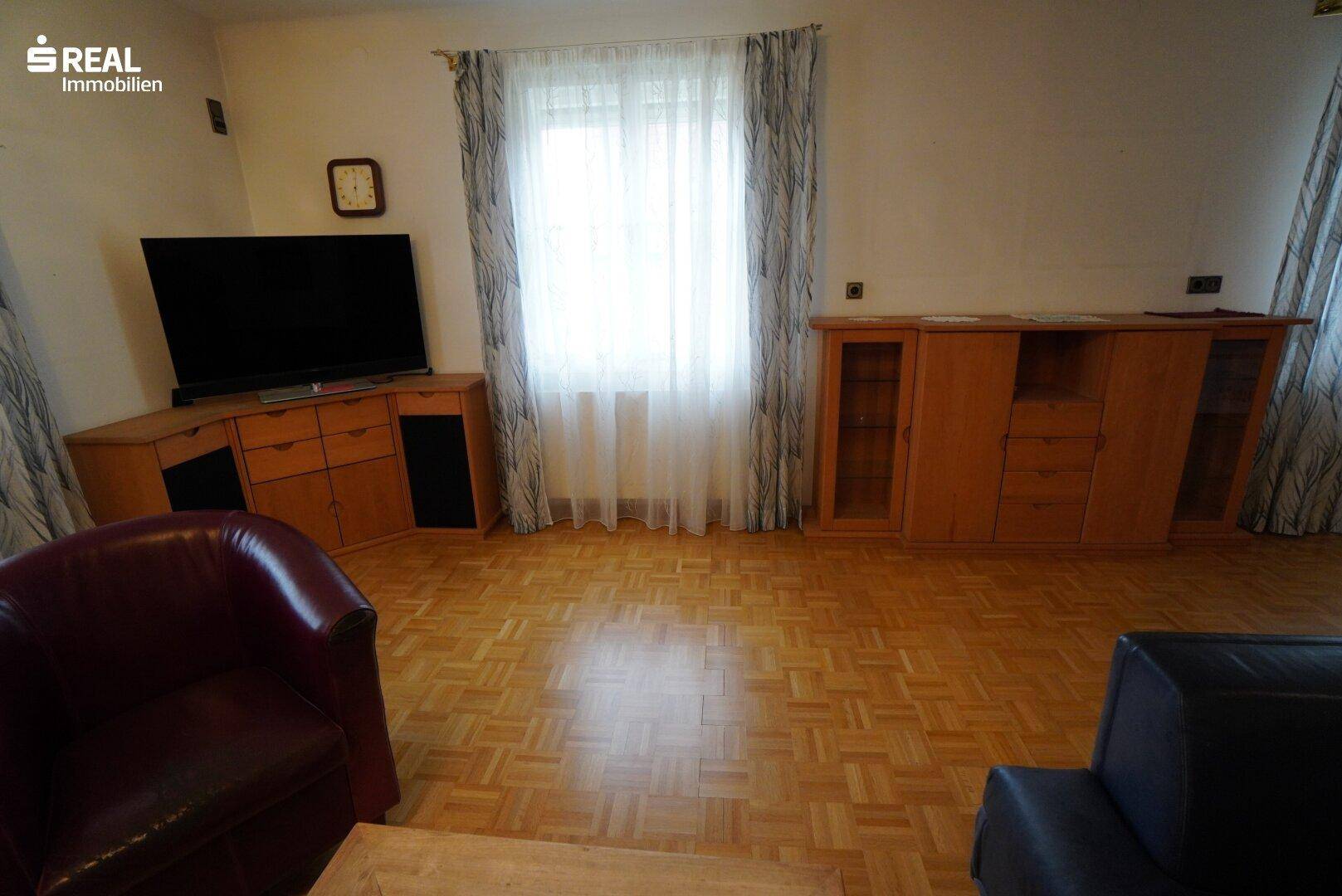 Wohnzimmer mit Parkettboden, großem Fenster und Sideboards aus Holz.
