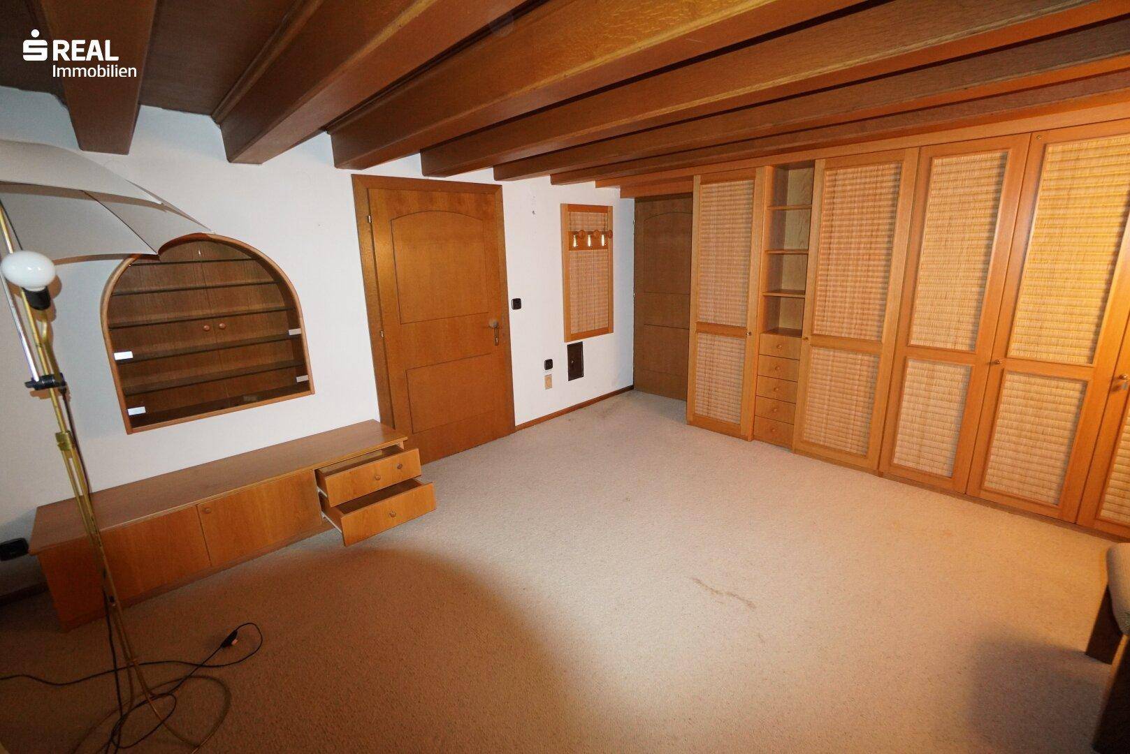 Schlafzimmer mit Teppichboden, Holzbalkendecke und maßgefertigten Einbauschränken.