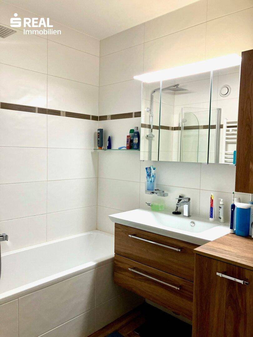 Badezimmer mit Badewanne, Waschbeckenunterschrank und Spiegelschrank.