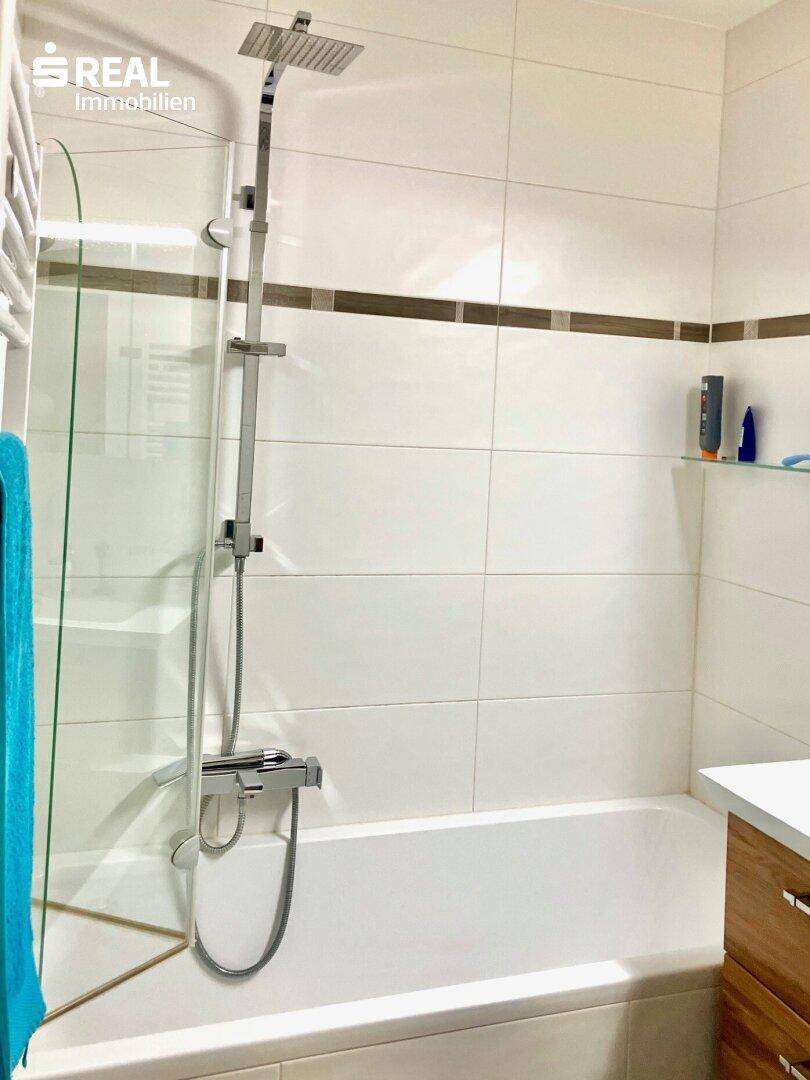 Badezimmer mit Badewanne, integrierter Dusche und modernen Fliesen.