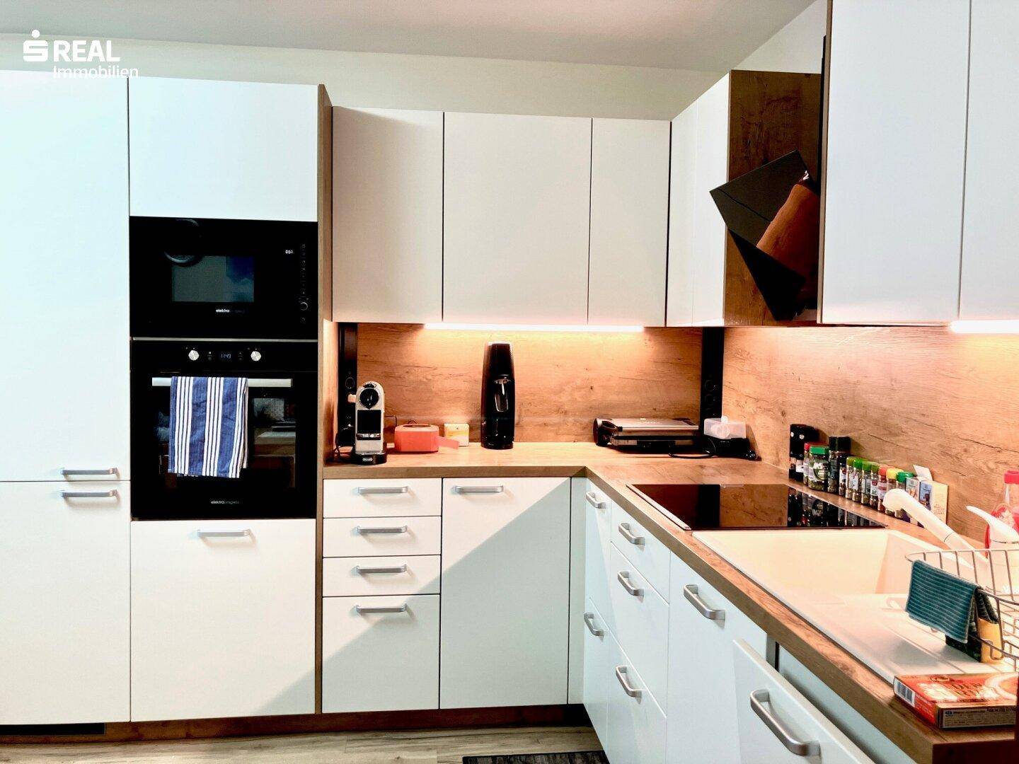 Moderne Einbauküche mit weißen Fronten, Holzdetails und integrierten Geräten.