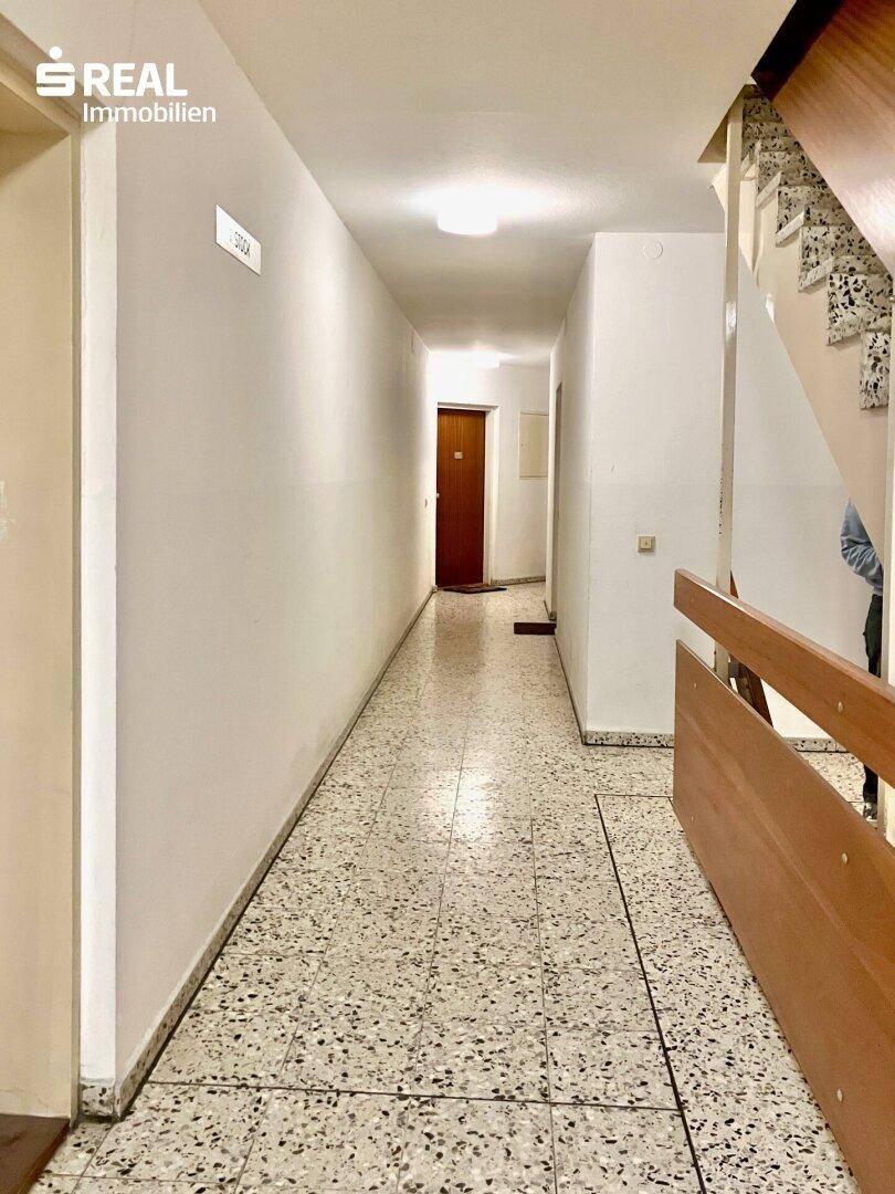 Langer Flur mit Terrazzoboden und Treppenaufgang, führt zu den Wohnbereichen.