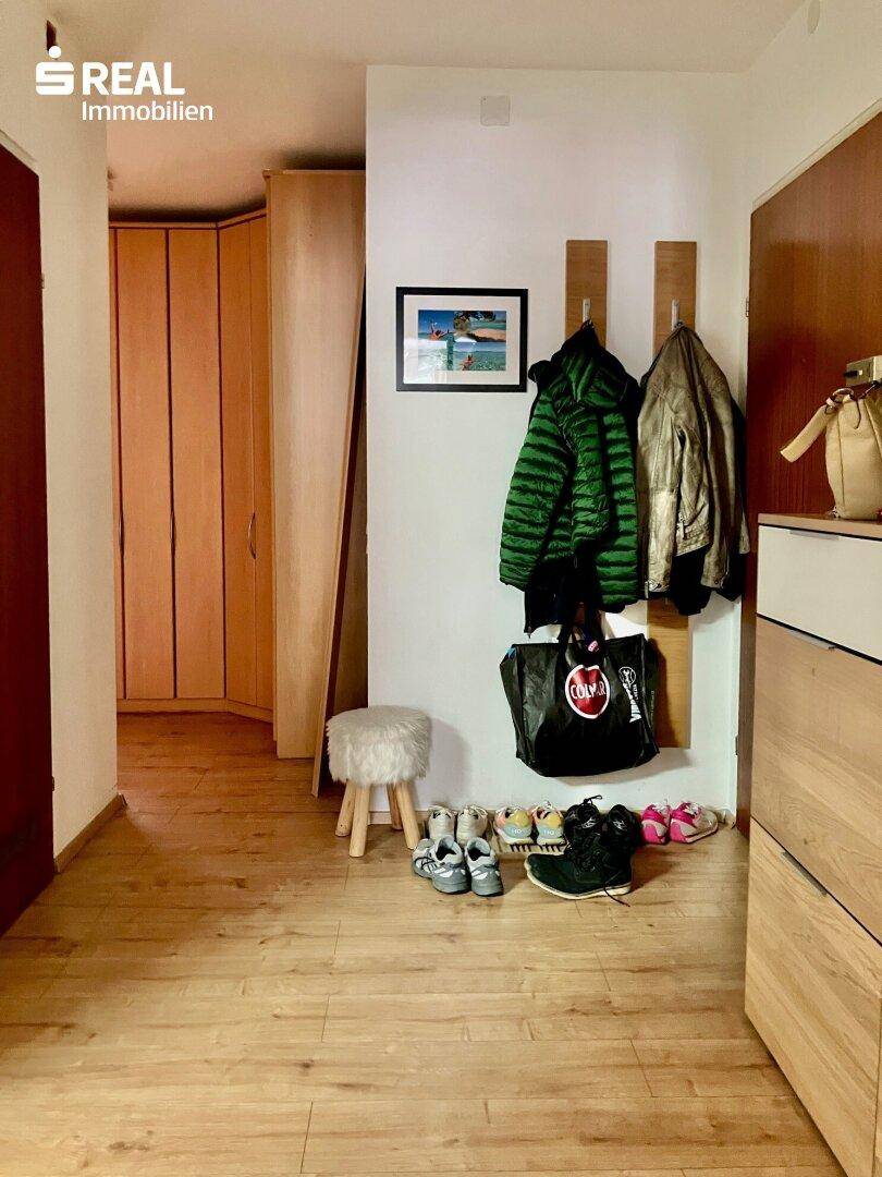 Eingangsbereich mit Garderobe, Schuhablage und hellem Holzboden.