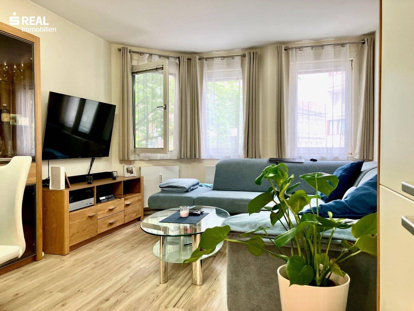 Gemütliches Wohnzimmer mit Sofa, Couchtisch und Blick ins Grüne durch die Fenster.