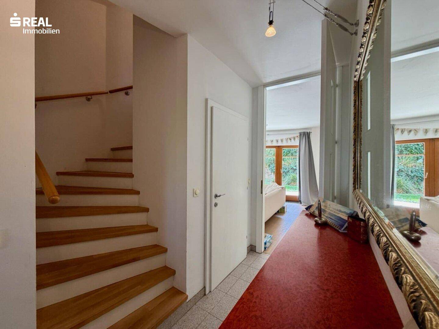 Heller Flur mit Holztreppe und großem Spiegel, der zum Wohnbereich führt.