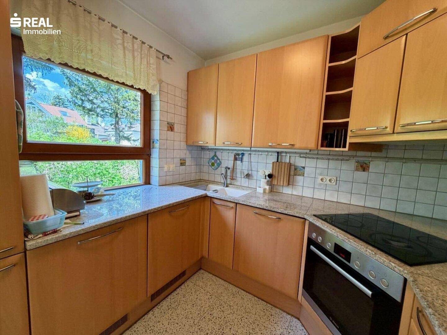 Funktionale Küche mit Holzschränken, Granitarbeitsplatte und Fenster mit Blick ins Grüne.