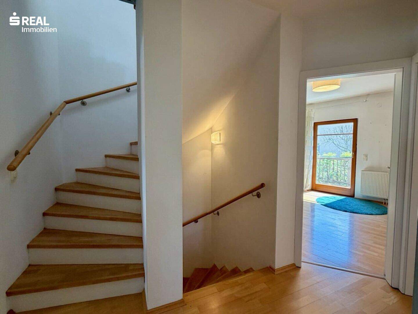 Heller Treppenaufgang mit Holzstufen und Zugang zu einem weiteren Zimmer mit Balkon.