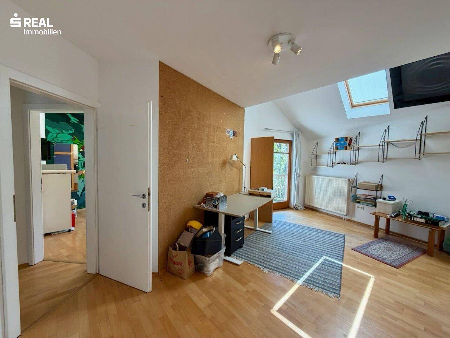 Helles Arbeitszimmer im Dachgeschoss mit Holzboden, Dachfenster und Korkwand.