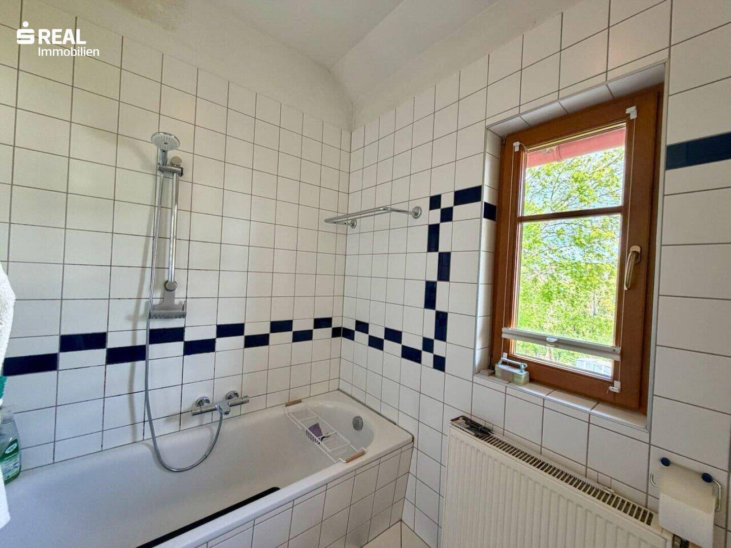 Badezimmer mit Badewanne, weißen Fliesen und Fenster, das Tageslicht hereinlässt.