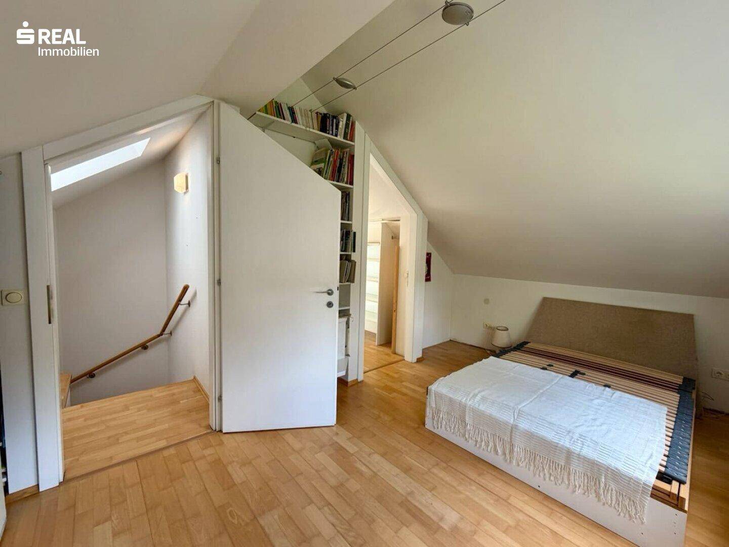 Schlafzimmer im Dachgeschoss mit Holzboden, Dachschrägen und integrierten Regalen.