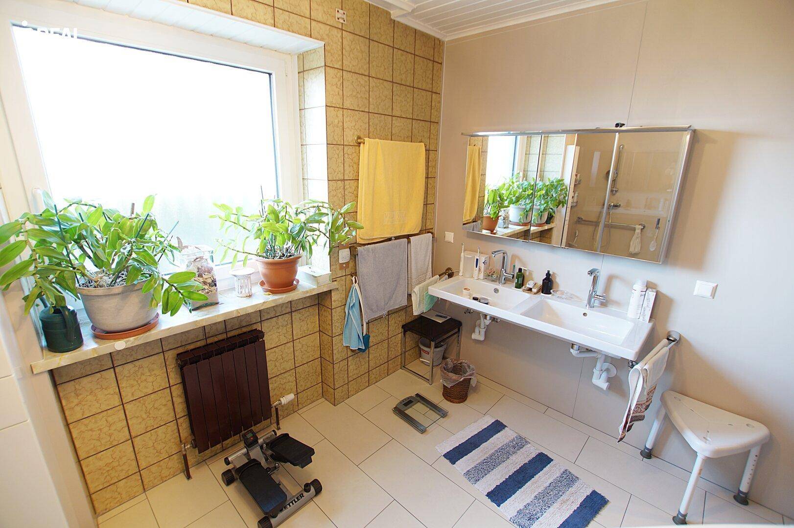 Helles Badezimmer mit Doppelwaschbecken, Spiegelschrank und Fenster, funktional eingerichtet.