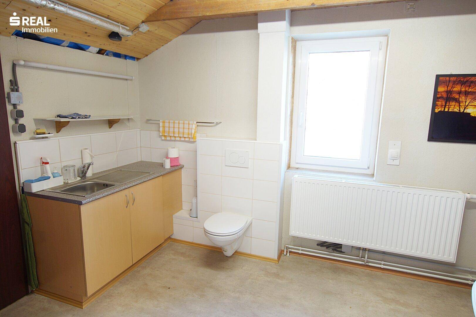 Einfaches WC im Dachgeschoss mit Waschbecken und Fenster, funktional und hell.