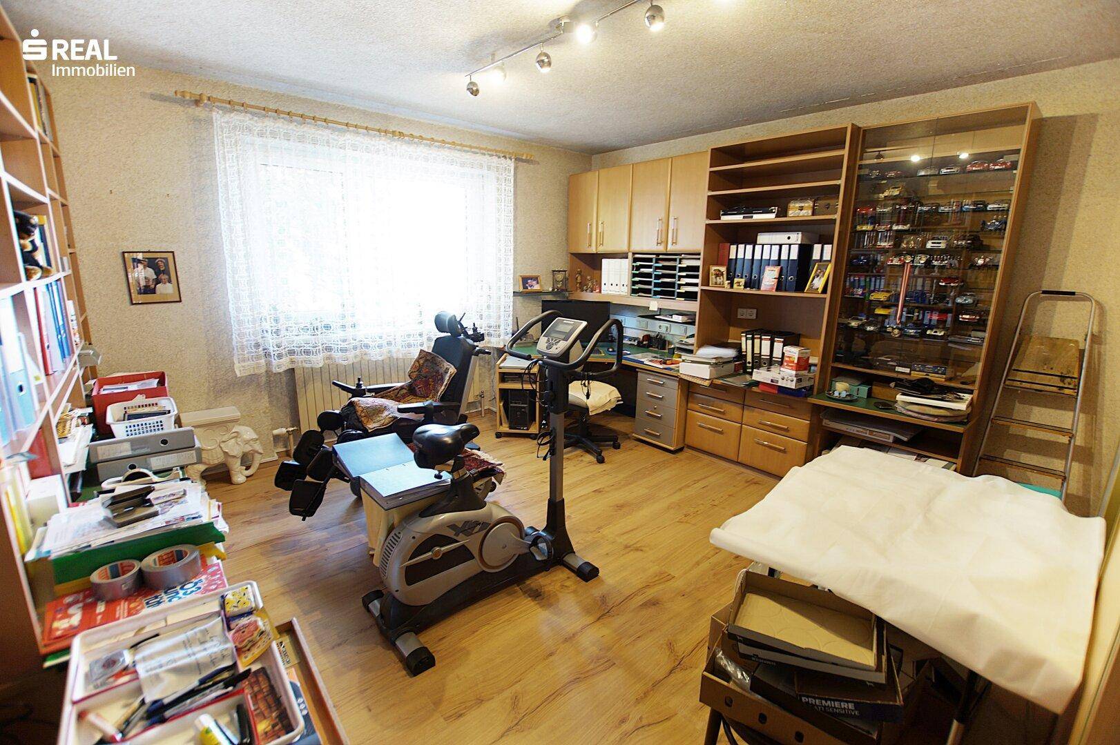 Helles Arbeitszimmer mit Schreibtisch, Regalen und Fitnessgeräten, ausgestattet für Produktivität und Bewegung.