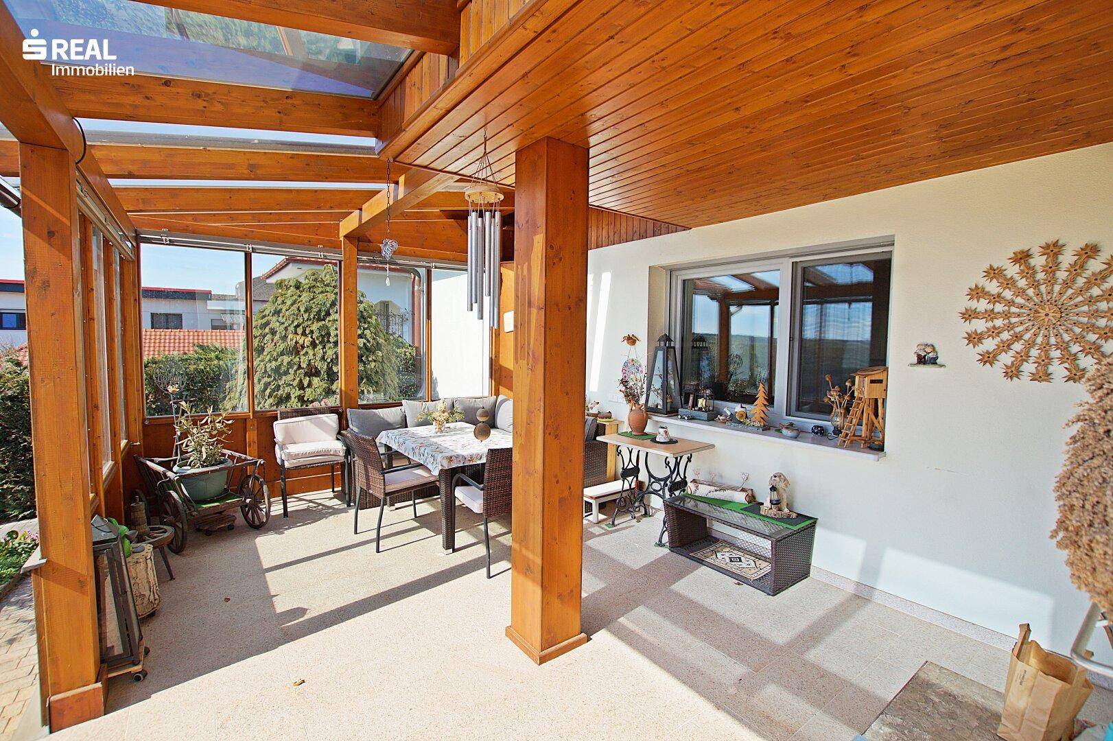 Gemütliche überdachte Terrasse mit Holzbalken und Blick auf den Garten, perfekt für Mahlzeiten im Freien.