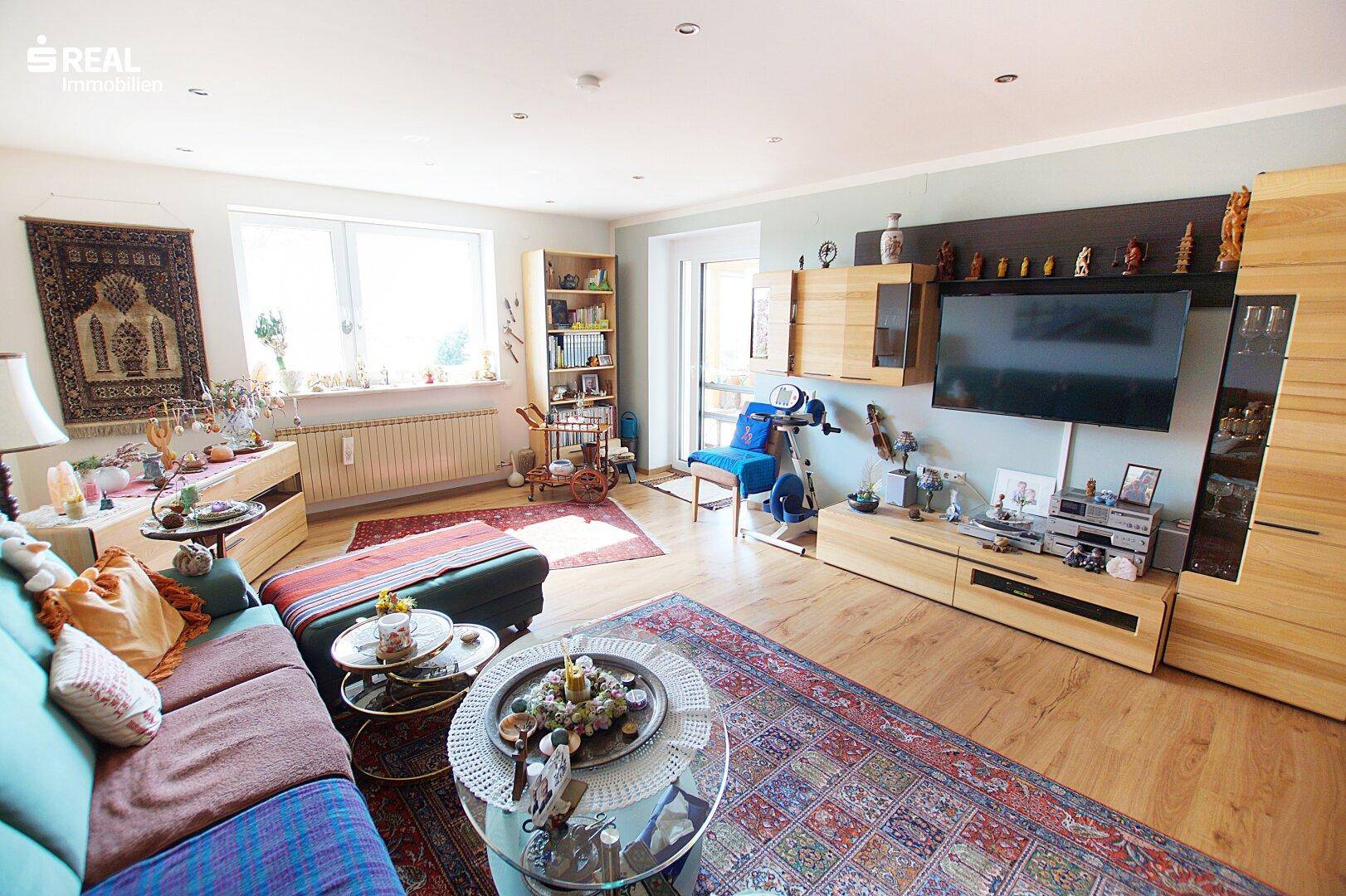 Helles Wohnzimmer mit Holzboden, bequemer Couch und Fernseher, dekoriert mit Teppichen und Möbeln.