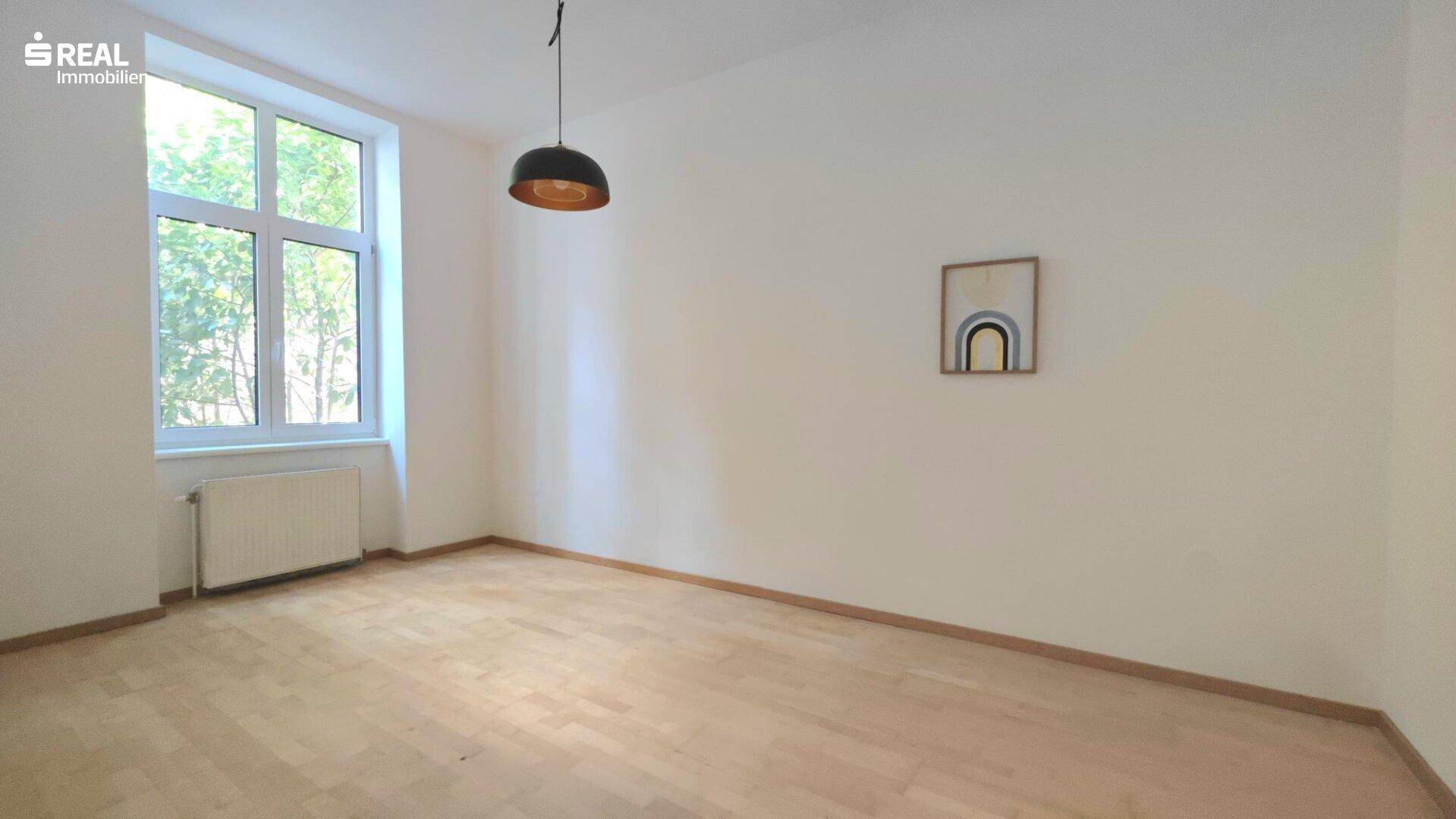 Geräumiges Schlafzimmer mit Parkettboden und viel Tageslicht durch das große Fenster.