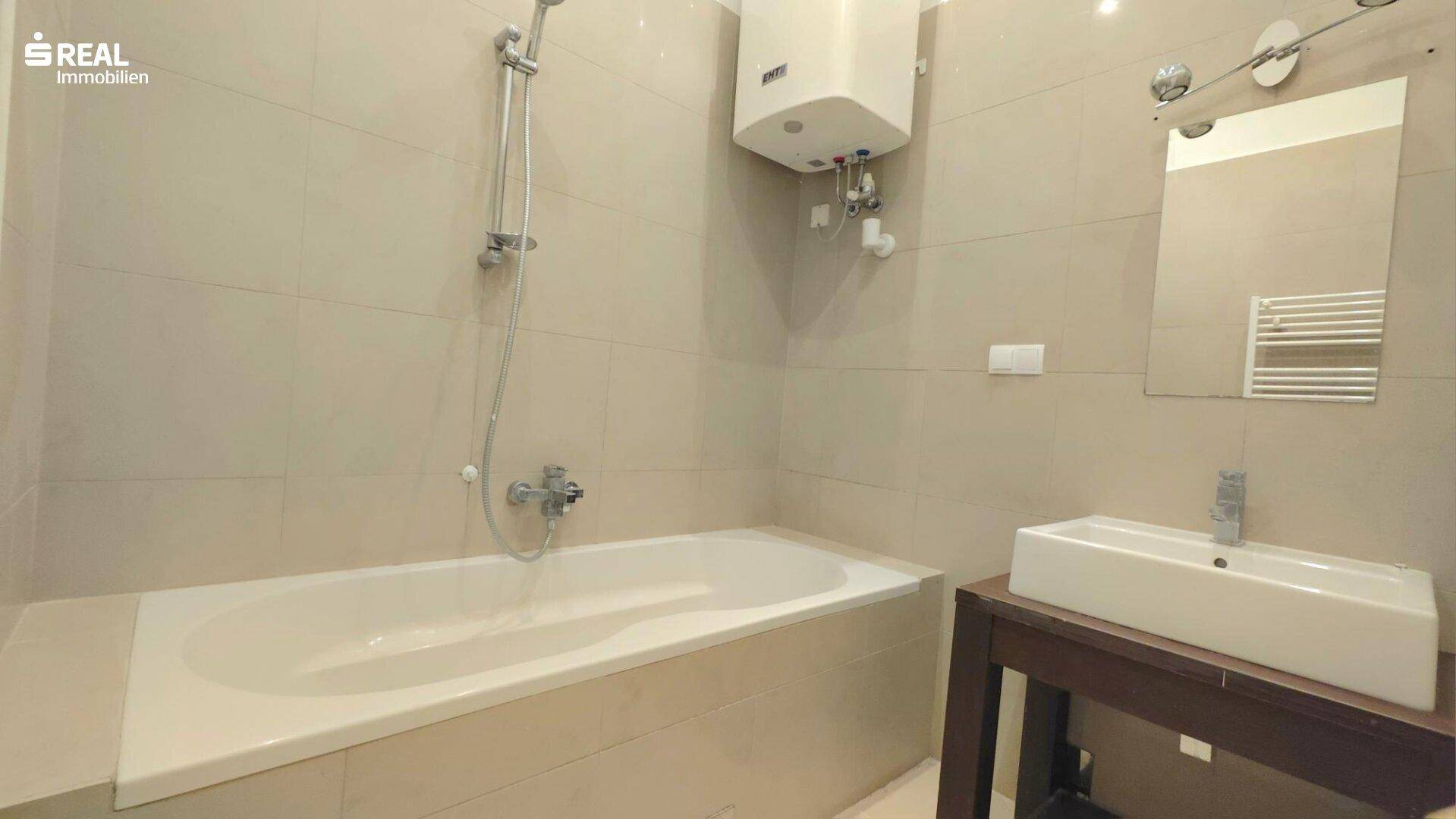 Modern gefliestes Badezimmer mit Badewanne, Waschbecken und Wandspiegel.