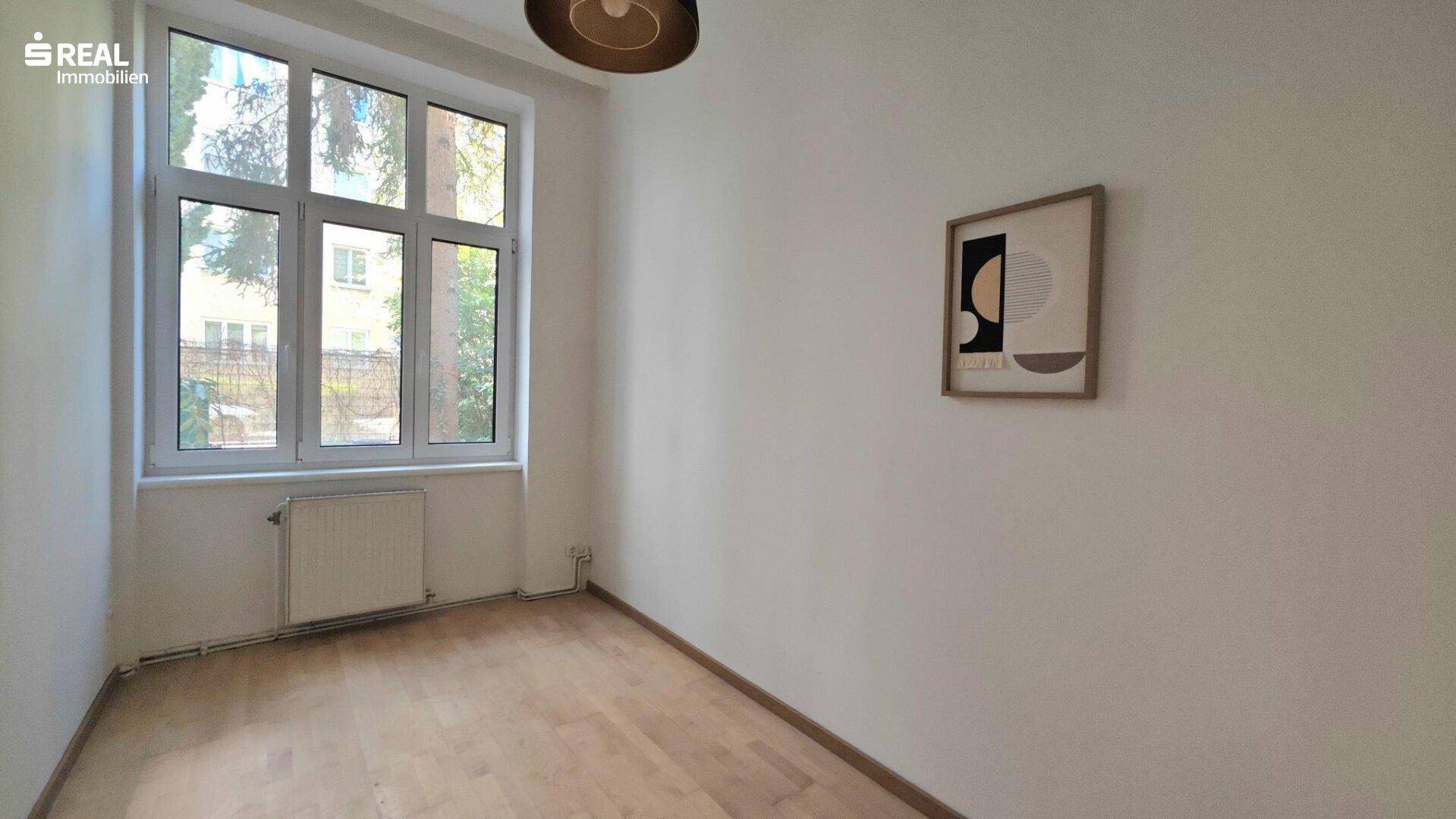 Helles Zimmer mit Holzboden, großem Fenster und Blick ins Grüne.