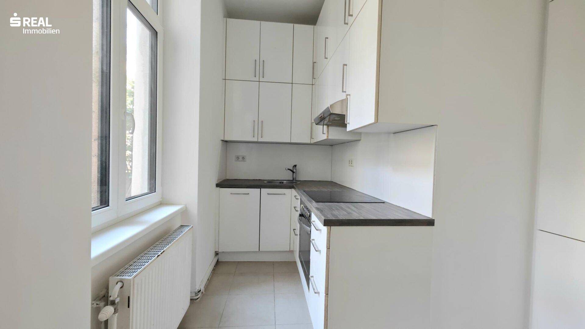Kompakte Küche mit weißen Fronten, Fliesenboden und Fenster für natürliches Licht.