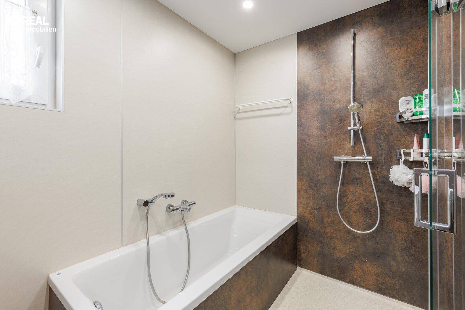 Modernisiertes Badezimmer mit Badewanne, Duschbereich und dunklen Akzentfliesen.