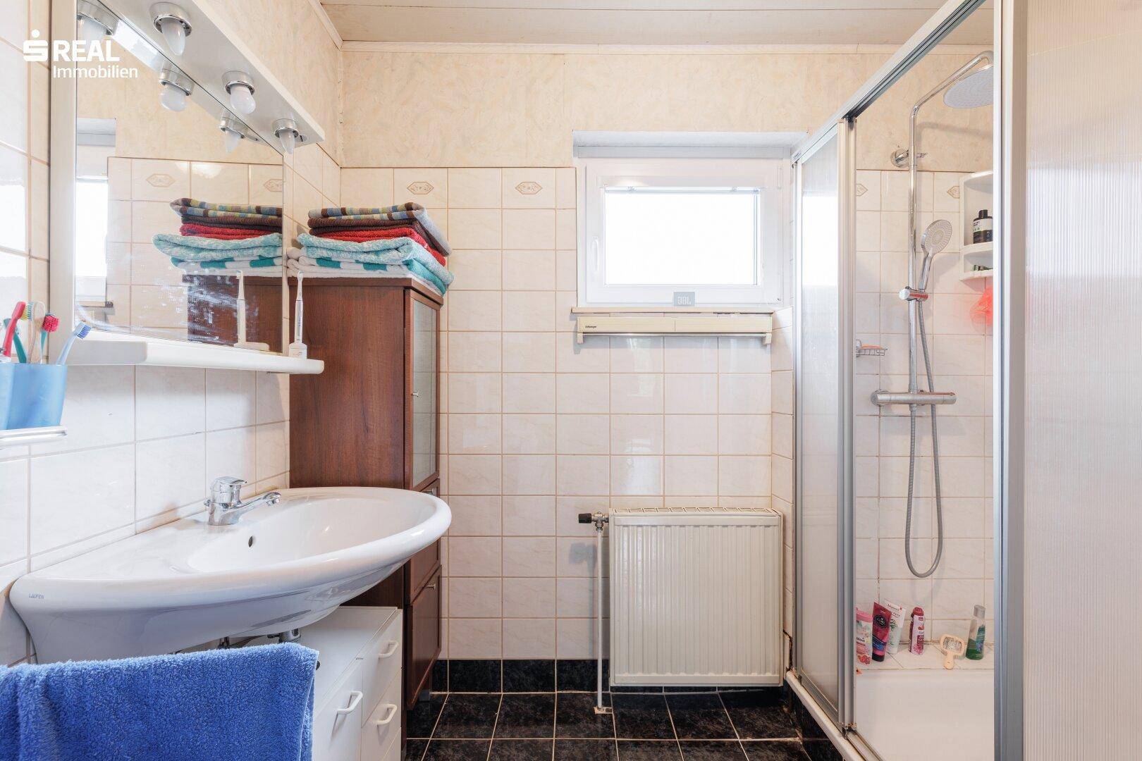 Badezimmer mit Dusche, Waschbecken, WC und Fenster für Belüftung.