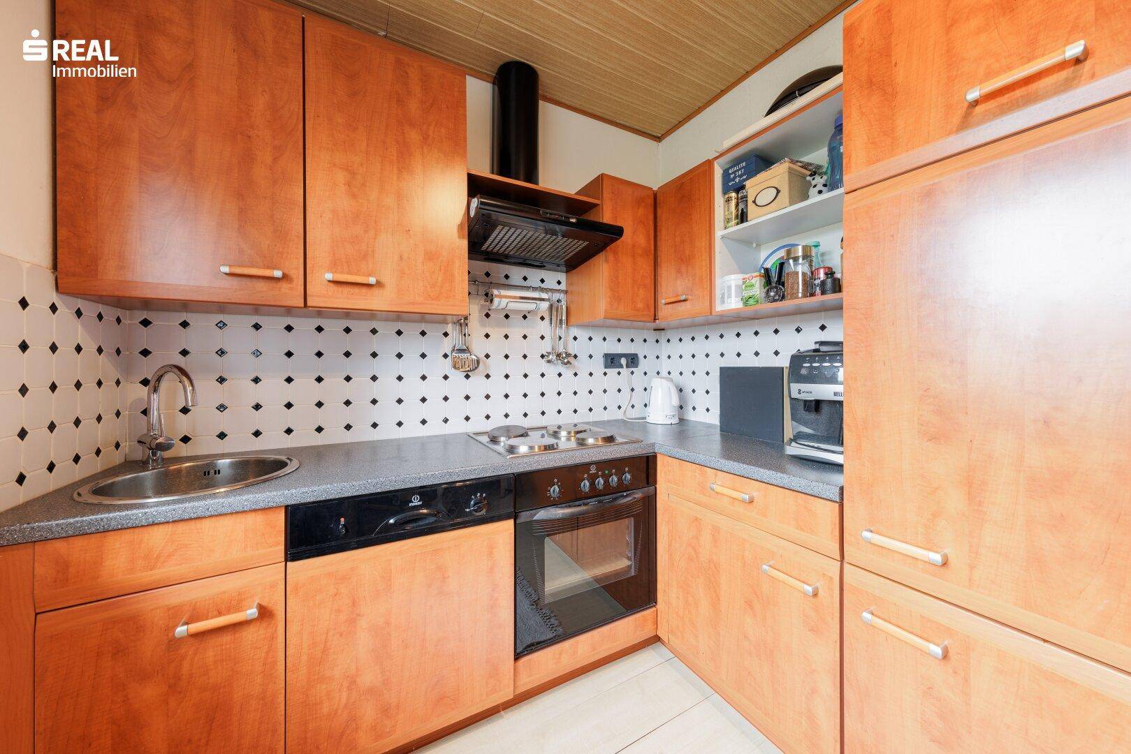 Kompakte Küche mit Holzschränken, Einbauherd und Fliesenrückwand.