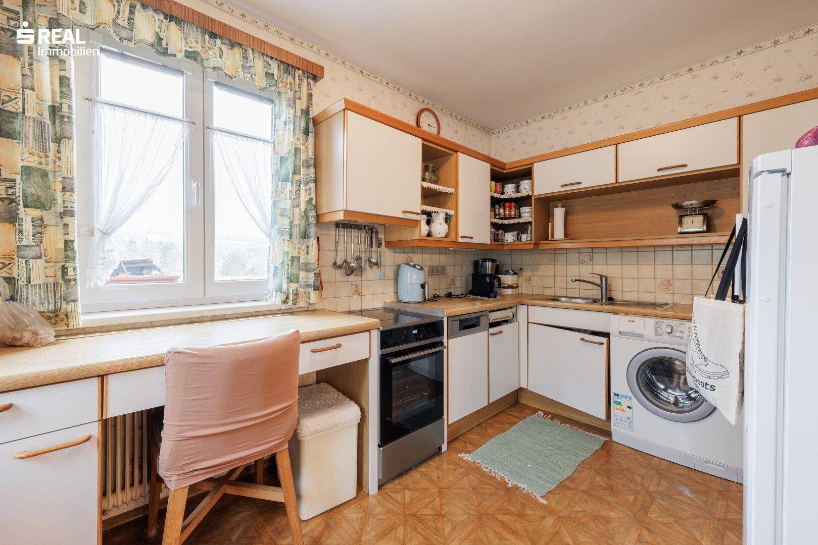 Funktionale Küche mit Einbaugeräten, Spüle und Waschmaschine unter dem Fenster.