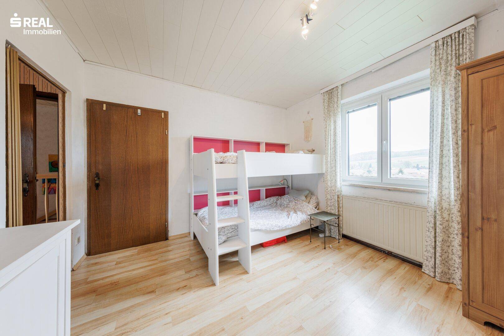 Kinderzimmer im Dachgeschoss mit Etagenbett, Holzschrank und Laminatboden.
