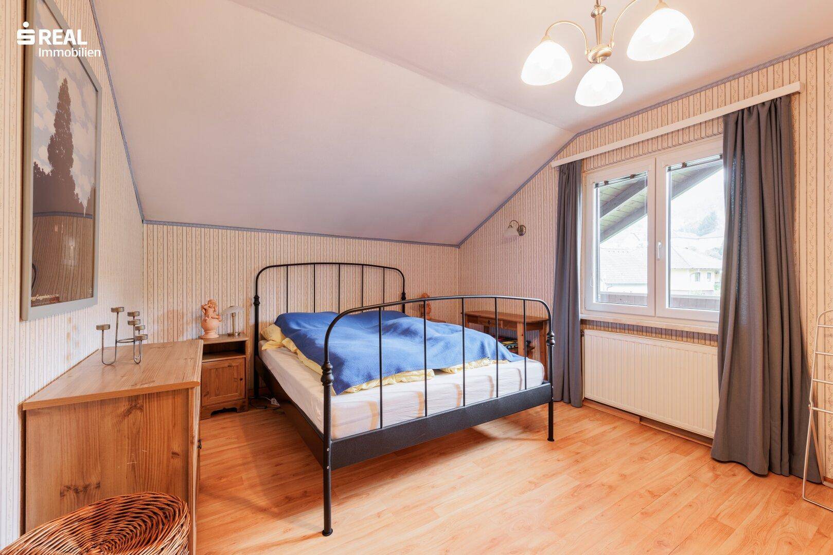 Schlafzimmer im Dachgeschoss mit Metallbett, Holzmöbeln und schrägen Wänden.