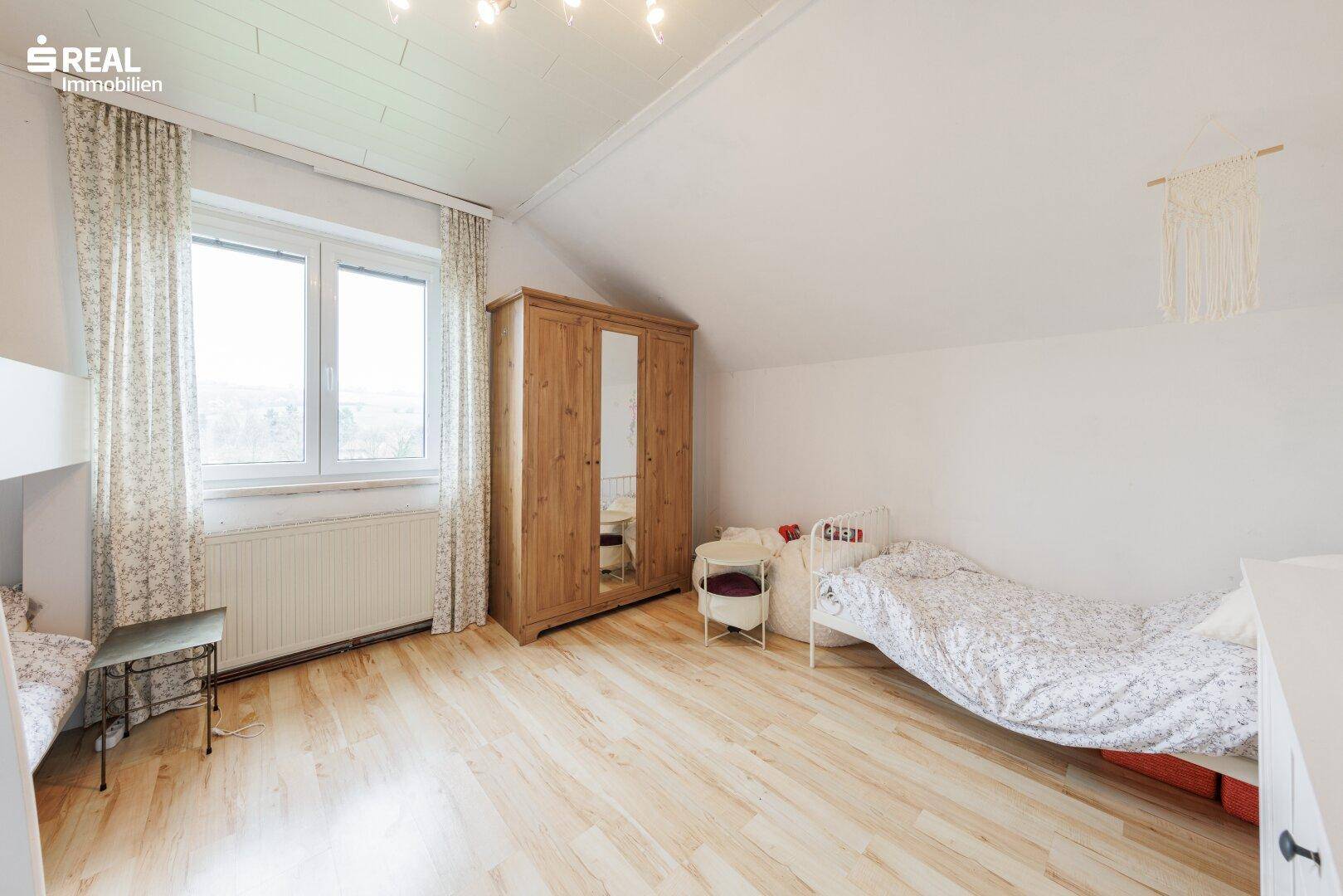 Helles Schlafzimmer im Dachgeschoss mit Holzkleiderschrank und Laminatboden.