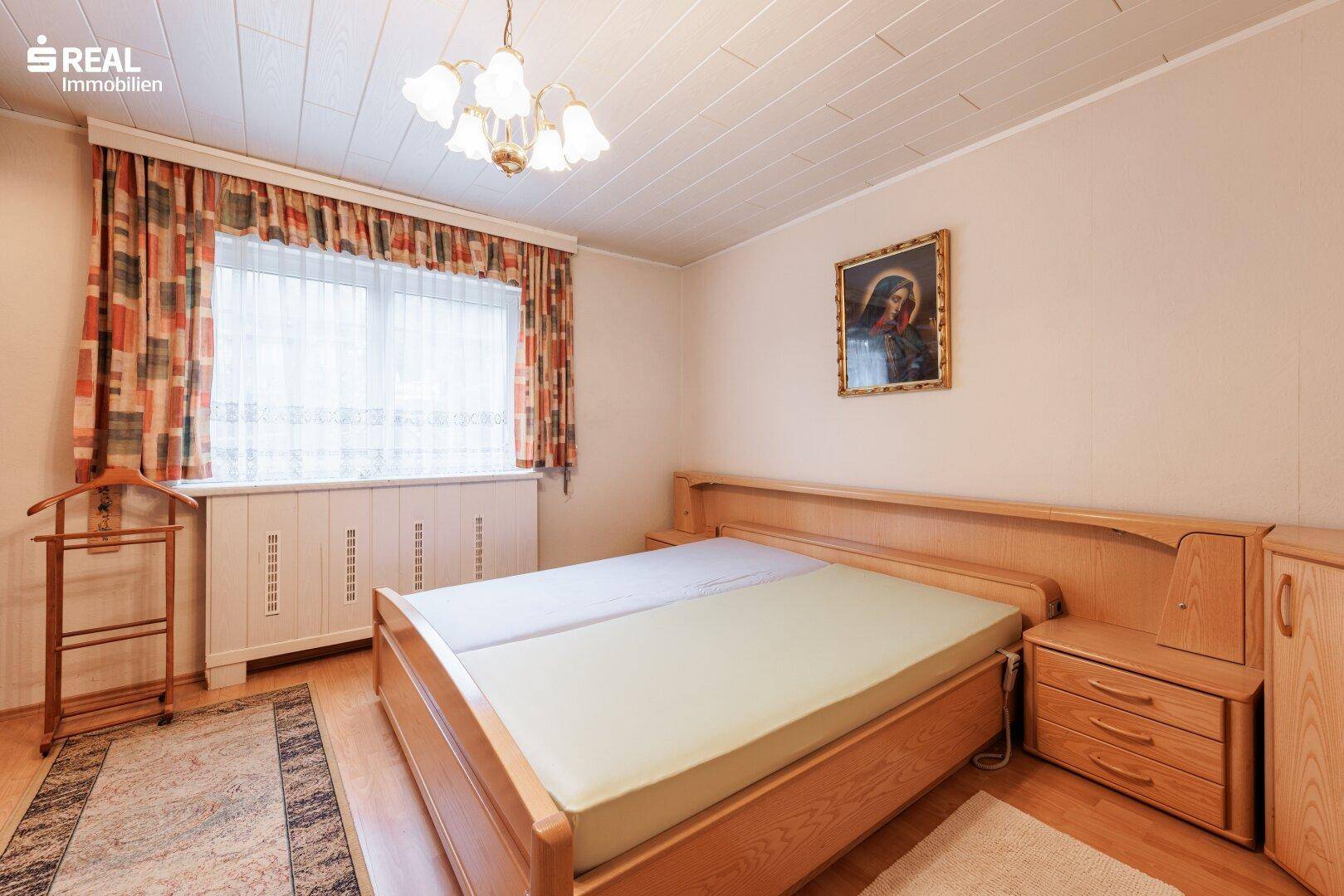 Schlafzimmer mit Doppelbett, Holzmöbeln und Fenster mit Blick ins Grüne.