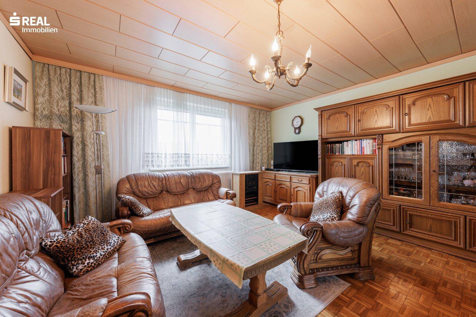 Gemütliches Wohnzimmer mit traditionellen Holzmöbeln, Ledersofas und Parkettboden.
