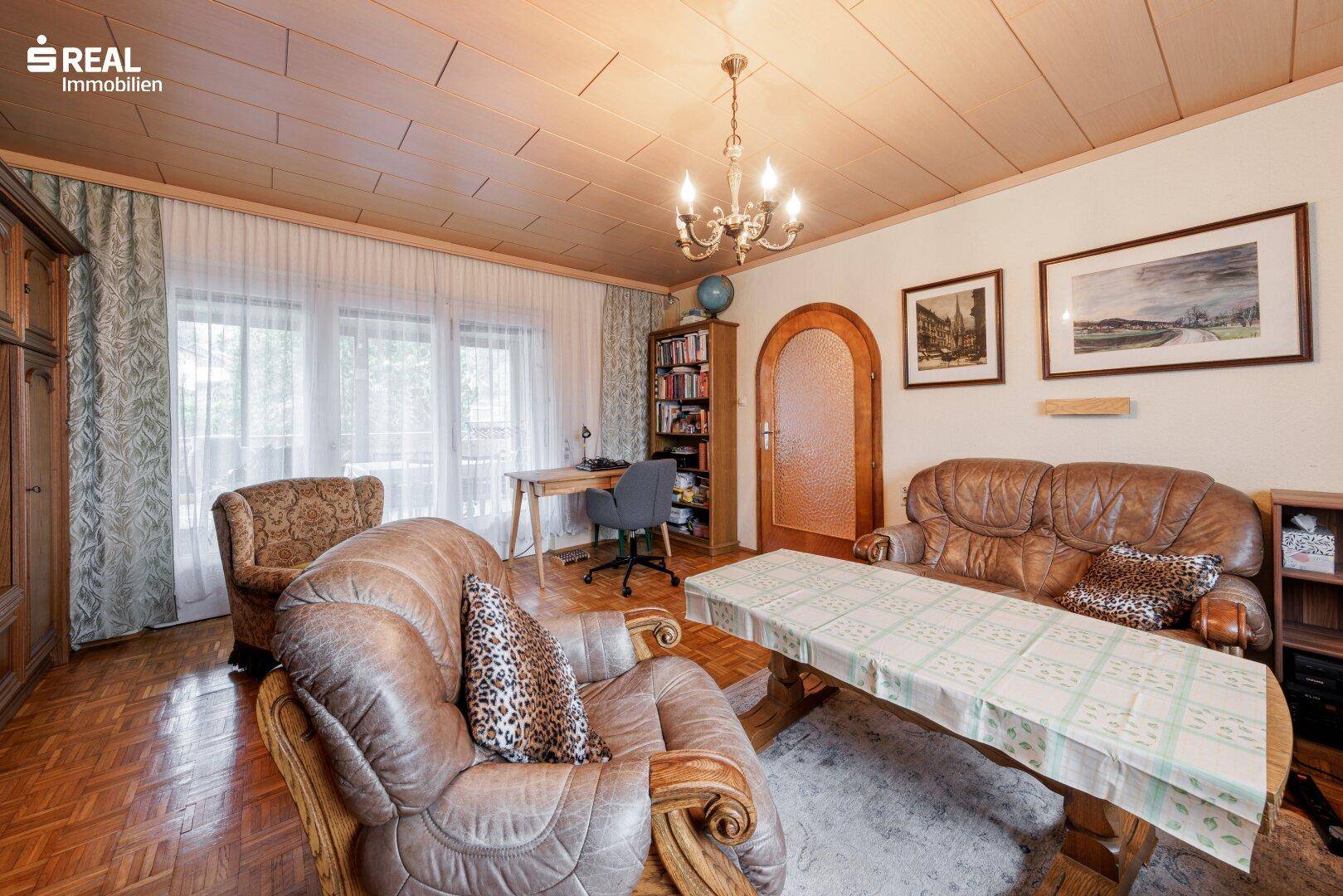 Wohnzimmer mit Ledersofas, Holzmöbeln und Blick auf den Schreibtischbereich.