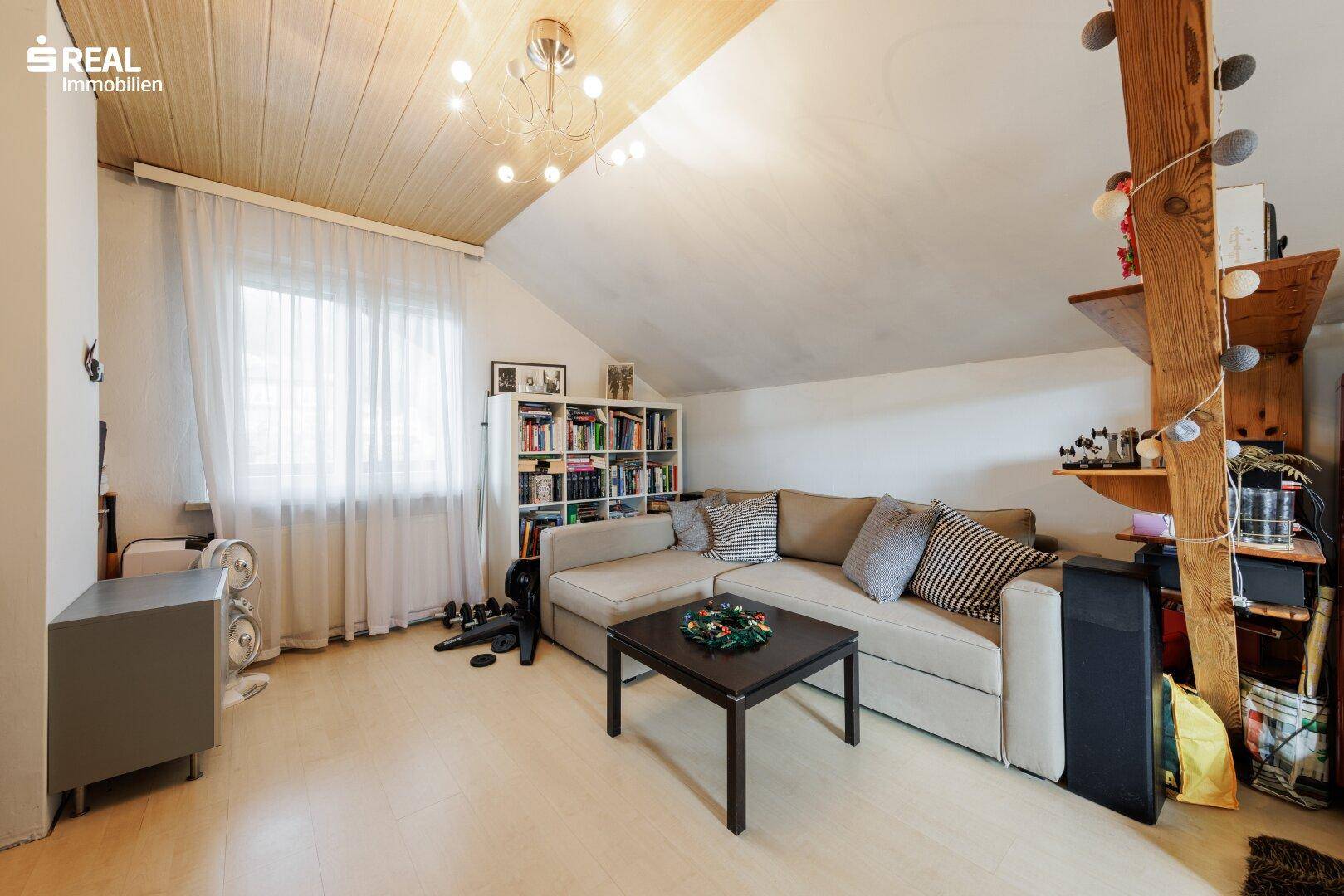 Gemütlicher Wohnbereich im Dachgeschoss mit Sofa, Bücherregal und Dachschrägen.