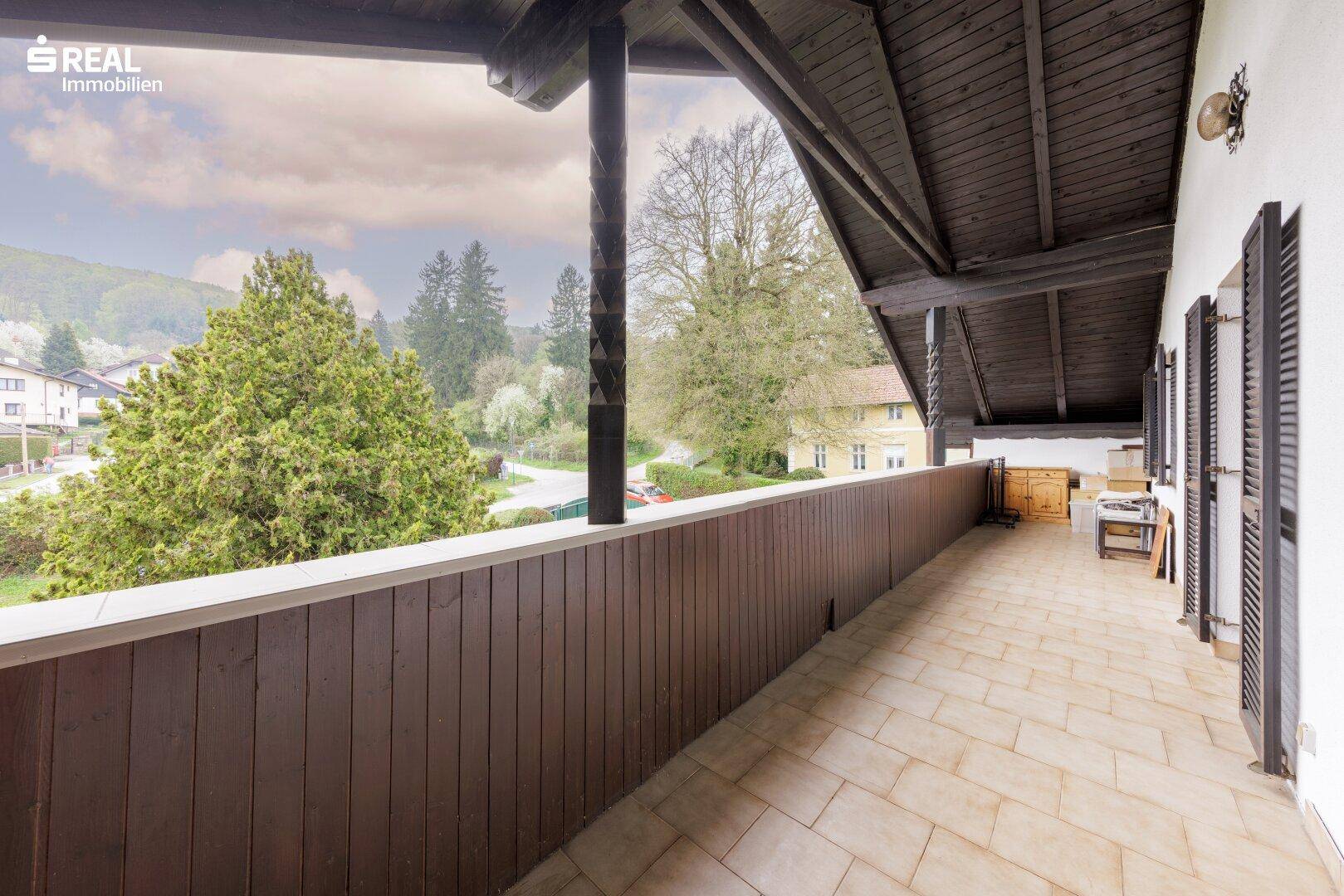 Langer, überdachter Balkon mit Fliesenboden und Holzgeländer, ideal zum Entspannen.