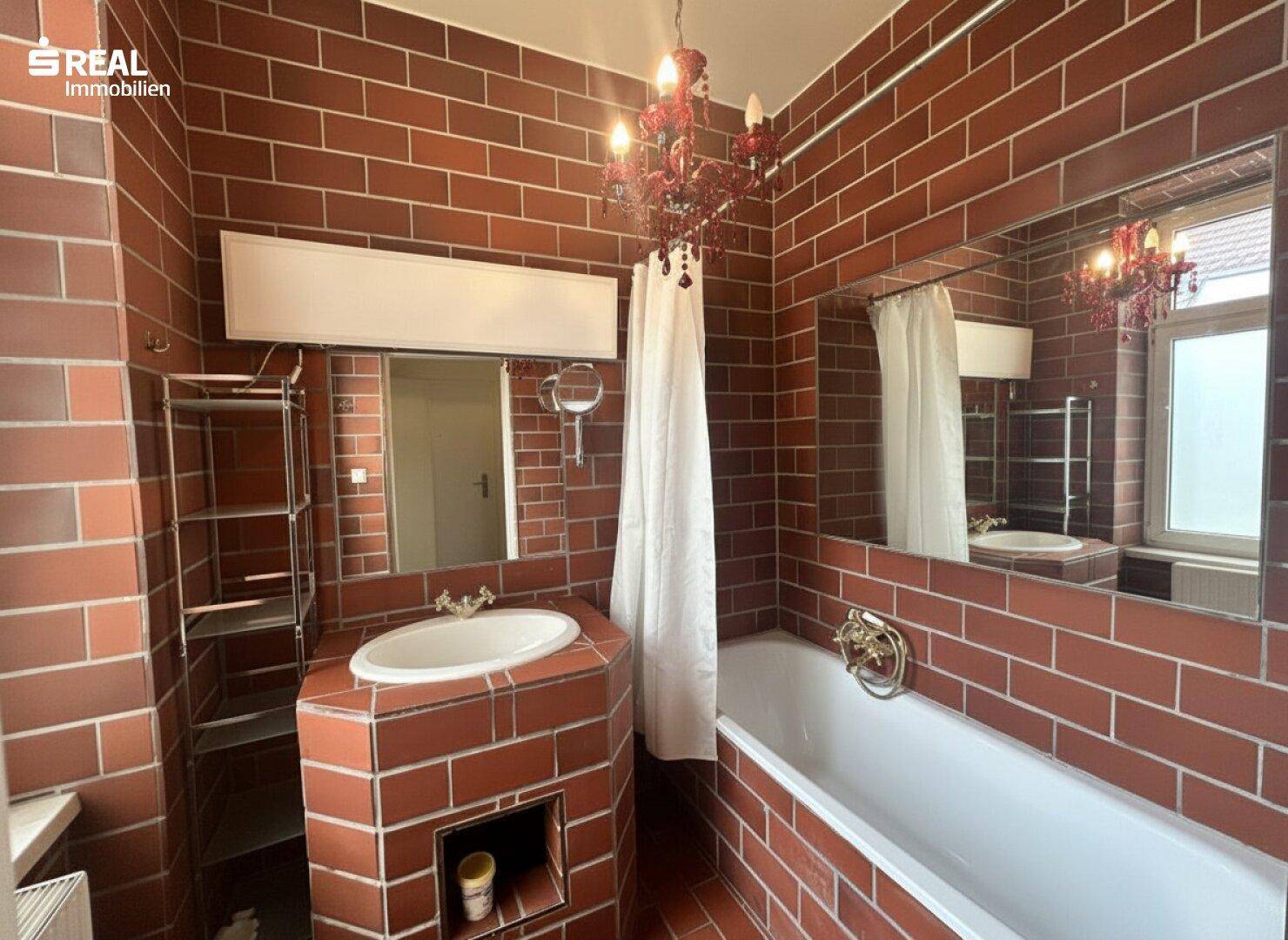 Badezimmer mit markanten roten Fliesen, Badewanne und einem Waschtisch mit Spiegel.